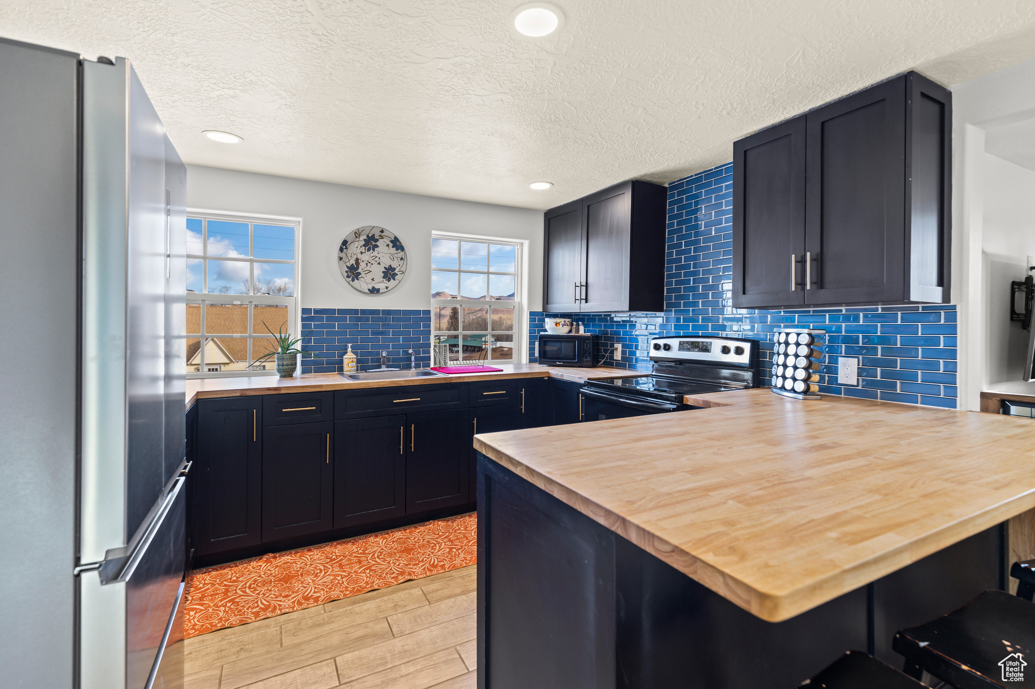 Kitchen with a kitchen bar, kitchen peninsula, butcher block countertops, appliances with stainless steel finishes, and tasteful backsplash