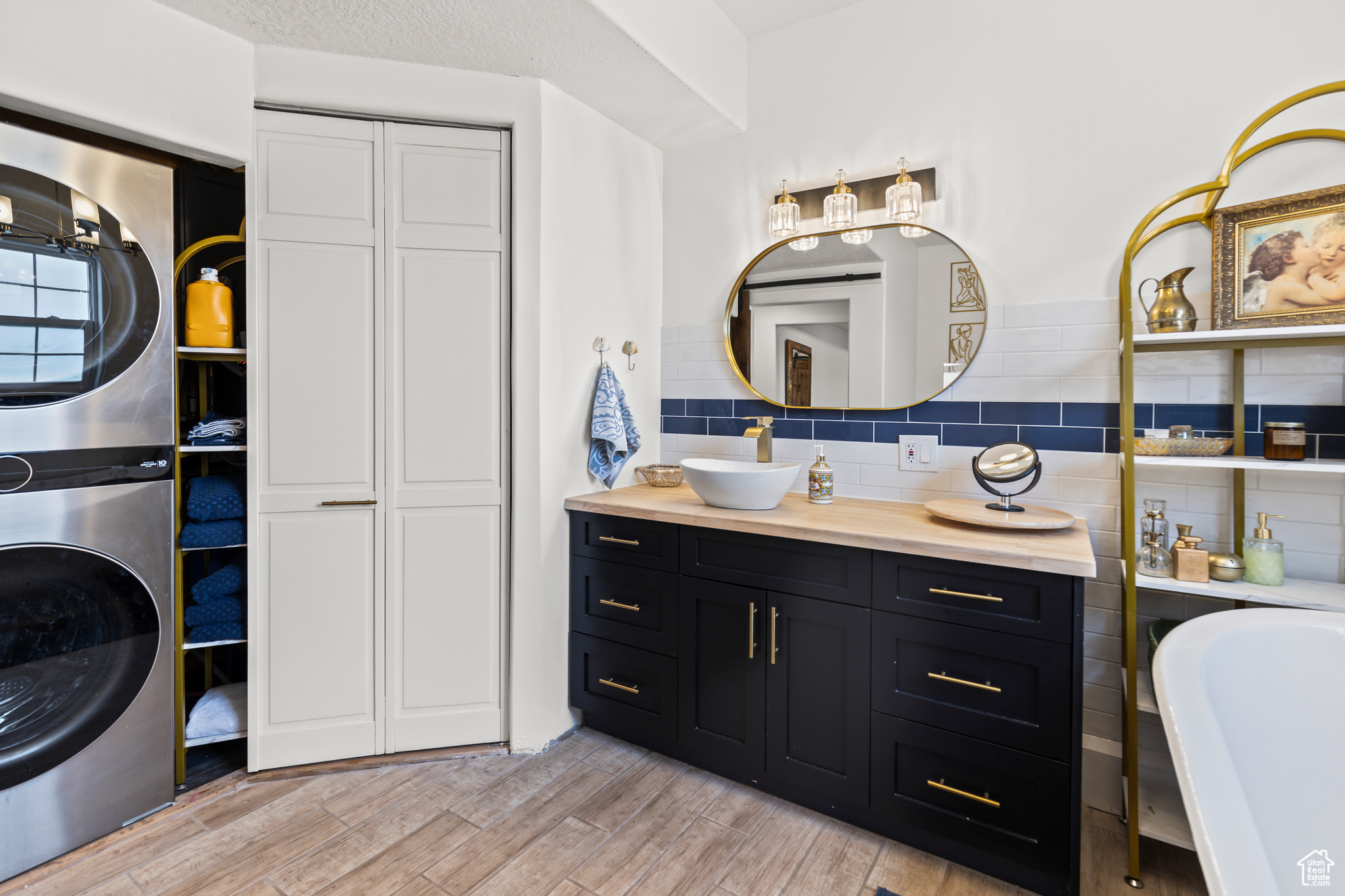 Bathroom with a textured ceiling, vanity, backsplash, a tub to relax in, and stacked washer and clothes dryer