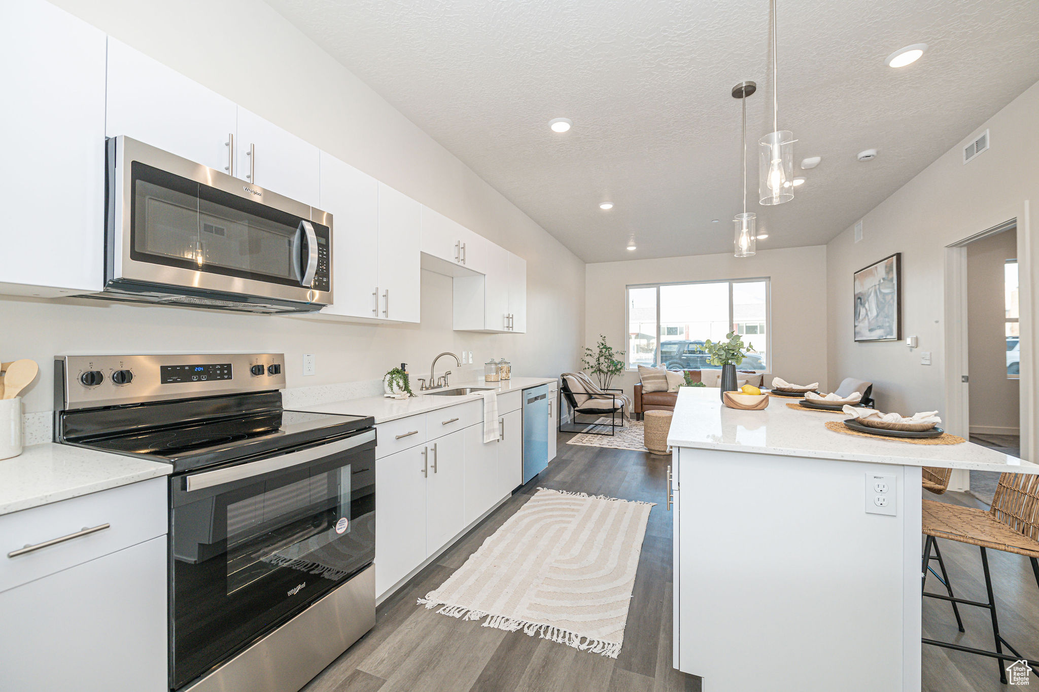 Kitchen with white cabinetry, stainless steel appliances, hanging light fixtures, a breakfast bar, and a center island