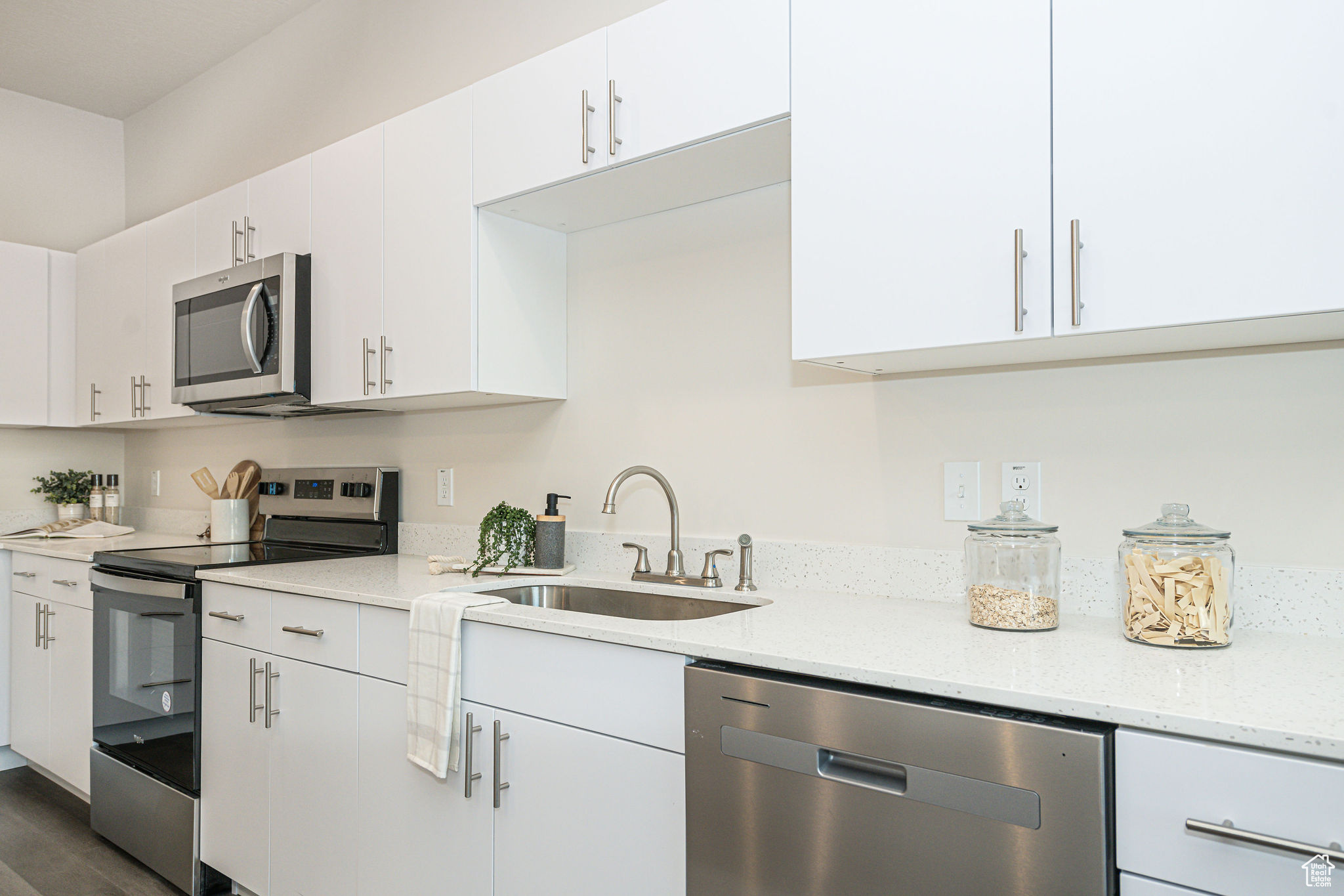 Kitchen featuring white cabinets, appliances with stainless steel finishes, dark wood-type flooring, sink, and light stone counters