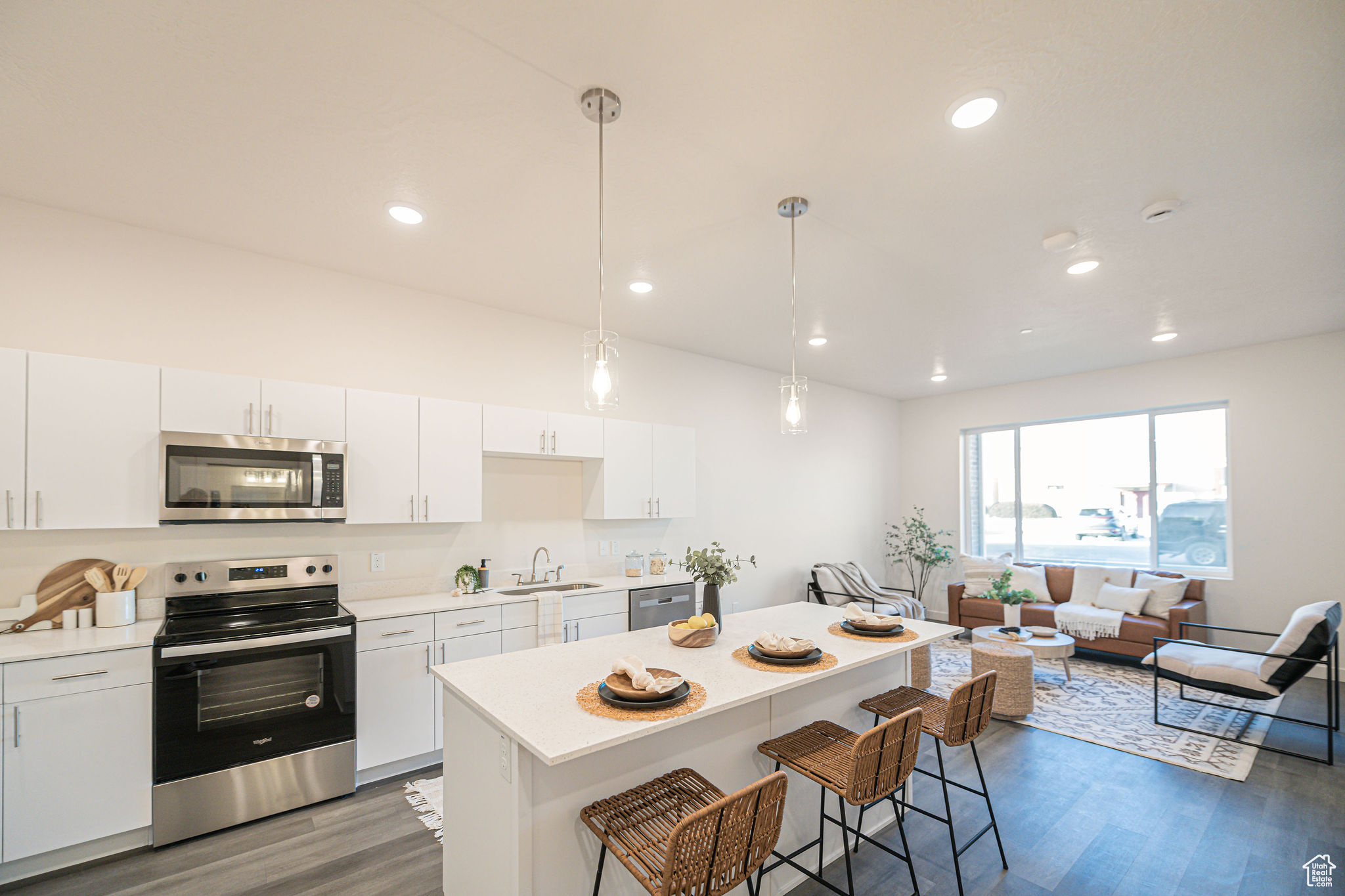 Kitchen with stainless steel appliances, sink, white cabinetry, and decorative light fixtures