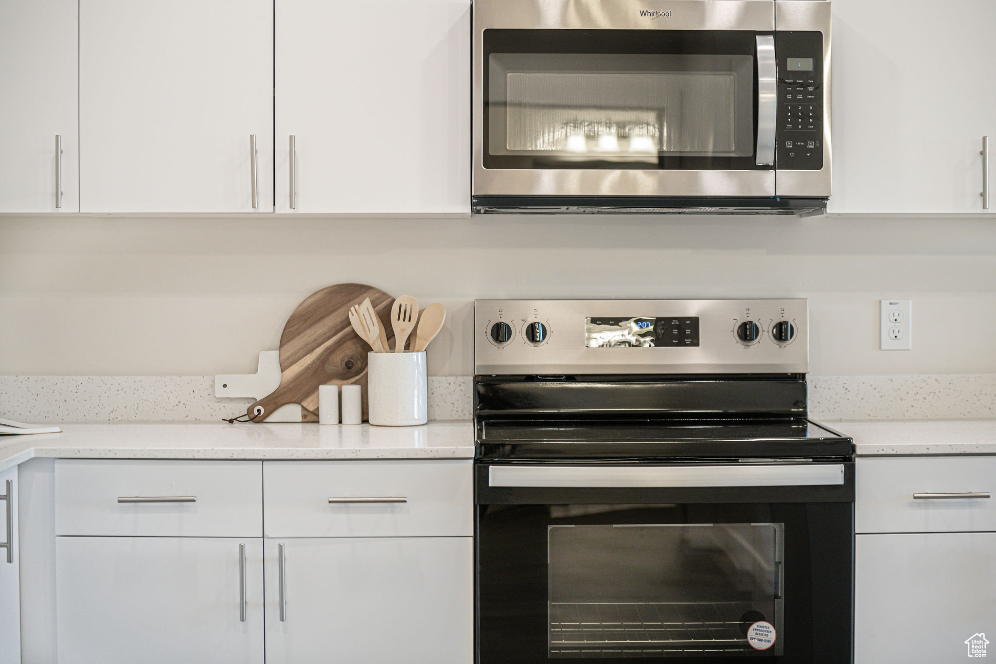 Kitchen with appliances with stainless steel finishes, white cabinets, and light stone counters