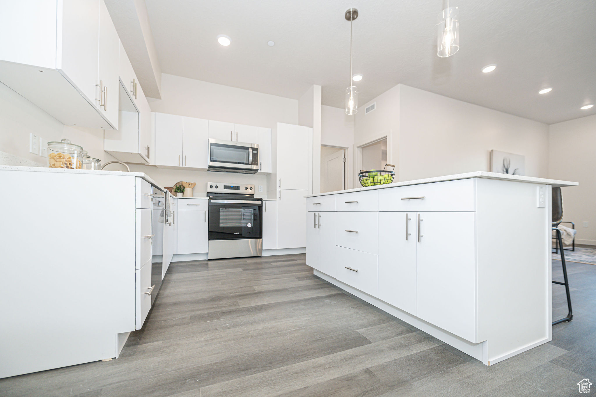 Kitchen with appliances with stainless steel finishes, a kitchen island, white cabinetry, and pendant lighting