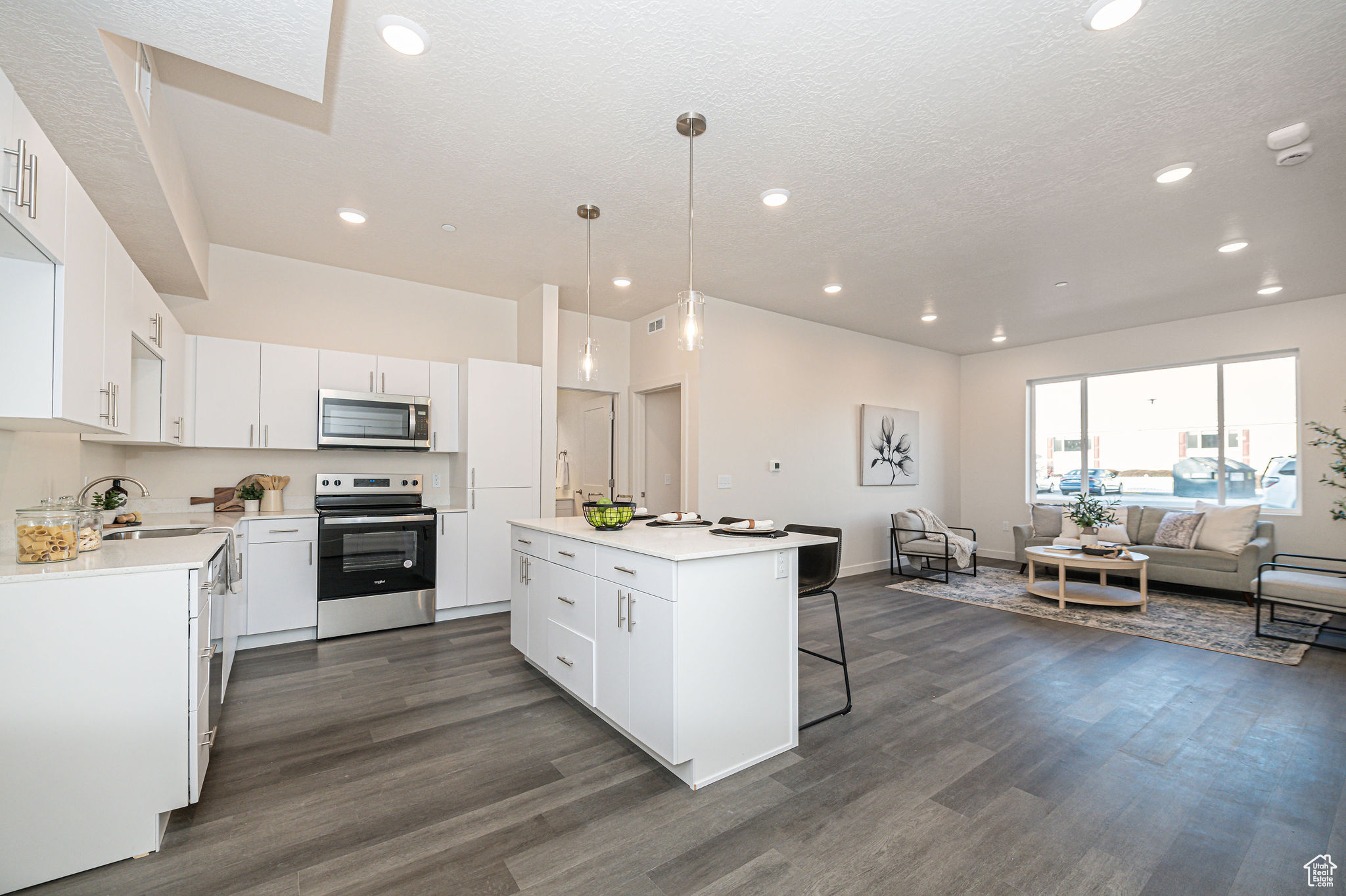 Kitchen with a kitchen island, hanging light fixtures, stainless steel appliances, white cabinets, and dark hardwood / wood-style flooring