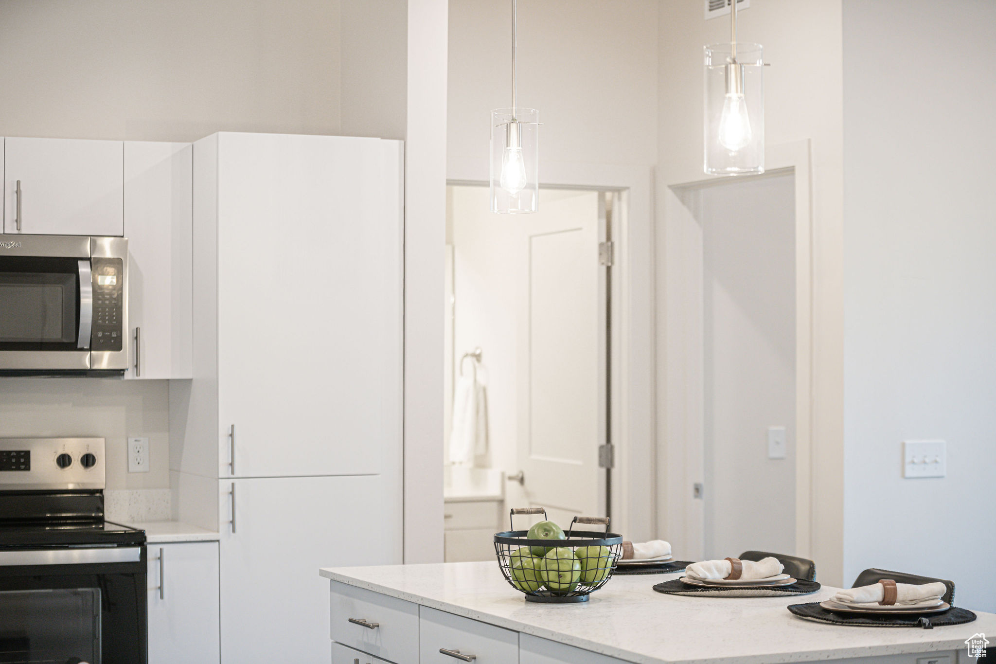 Kitchen with pendant lighting, light stone countertops, white cabinetry, and stainless steel appliances