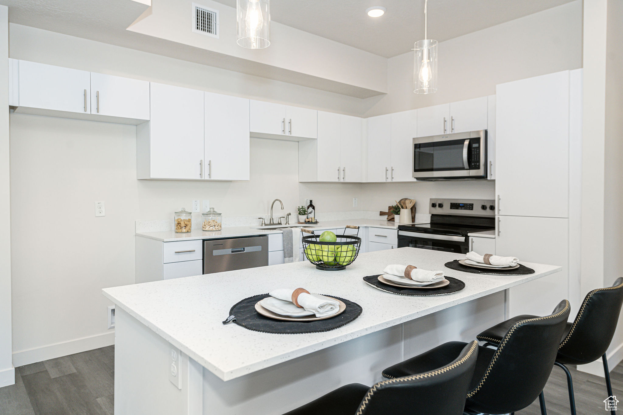 Kitchen featuring appliances with stainless steel finishes, a center island, dark wood-type flooring, white cabinetry, and hanging light fixtures