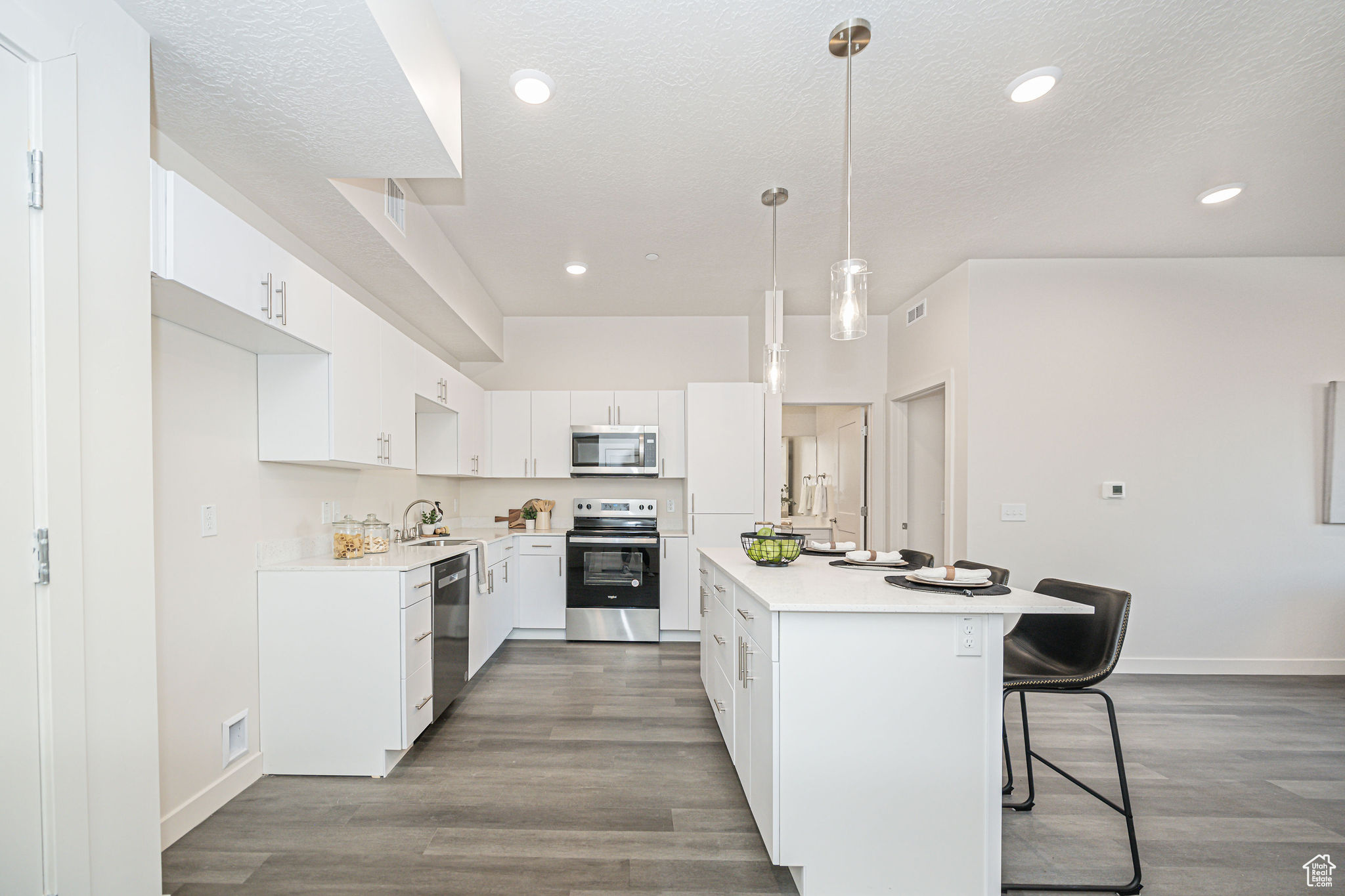 Kitchen with white cabinetry, a kitchen bar, appliances with stainless steel finishes, wood-type flooring, and pendant lighting