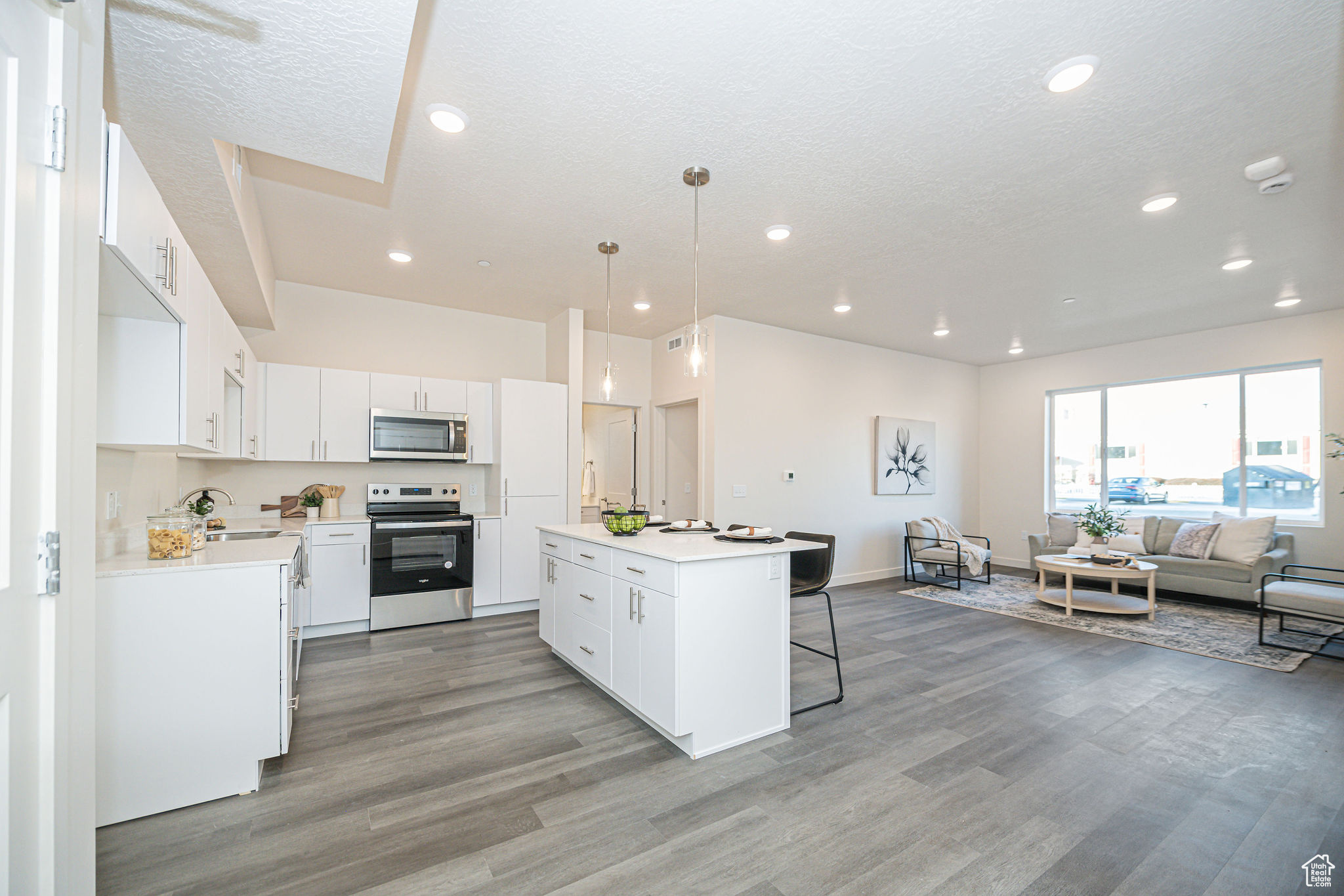 Kitchen featuring decorative light fixtures, a center island, sink, white cabinetry, and appliances with stainless steel finishes