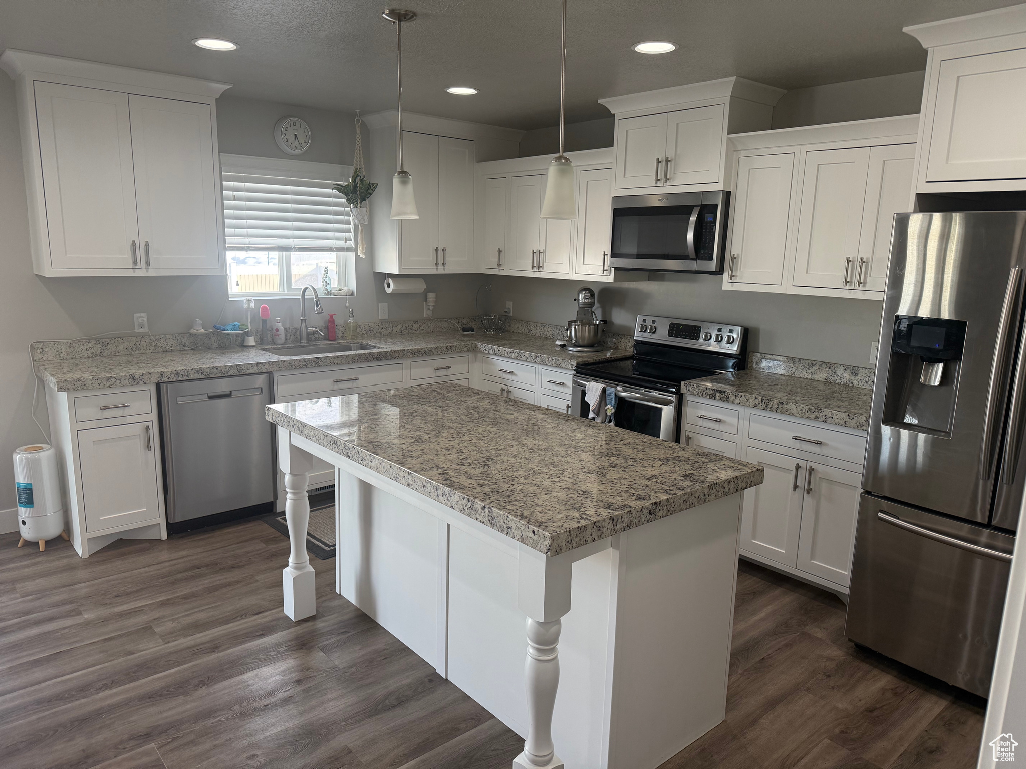 Kitchen with appliances with stainless steel finishes, decorative light fixtures, a kitchen island, white cabinets, and sink