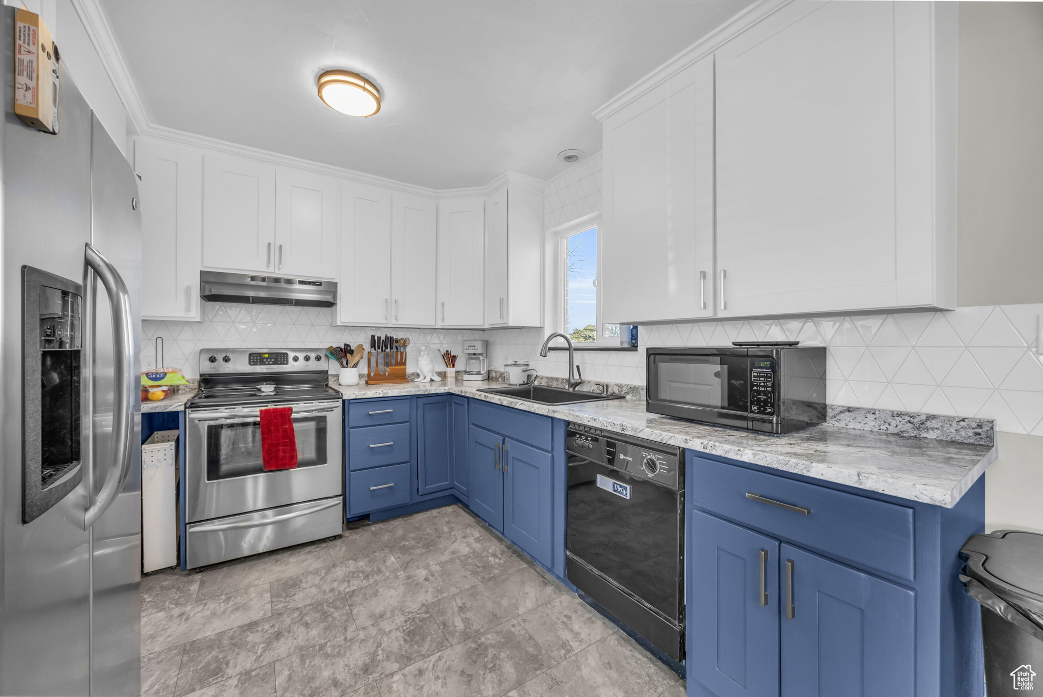 Kitchen with black appliances, white cabinetry, blue cabinetry, backsplash, and sink