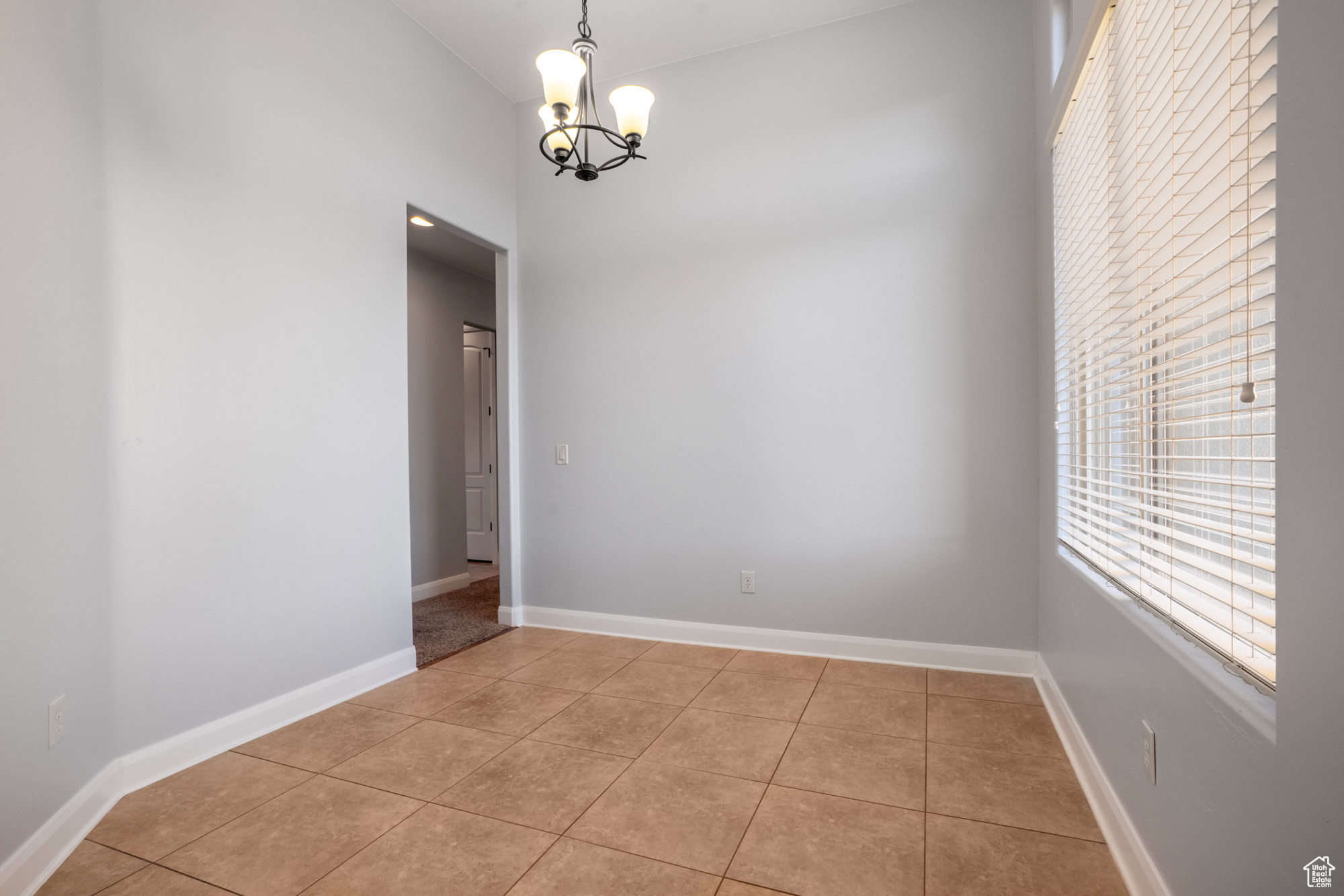 Tiled spare room featuring an inviting chandelier