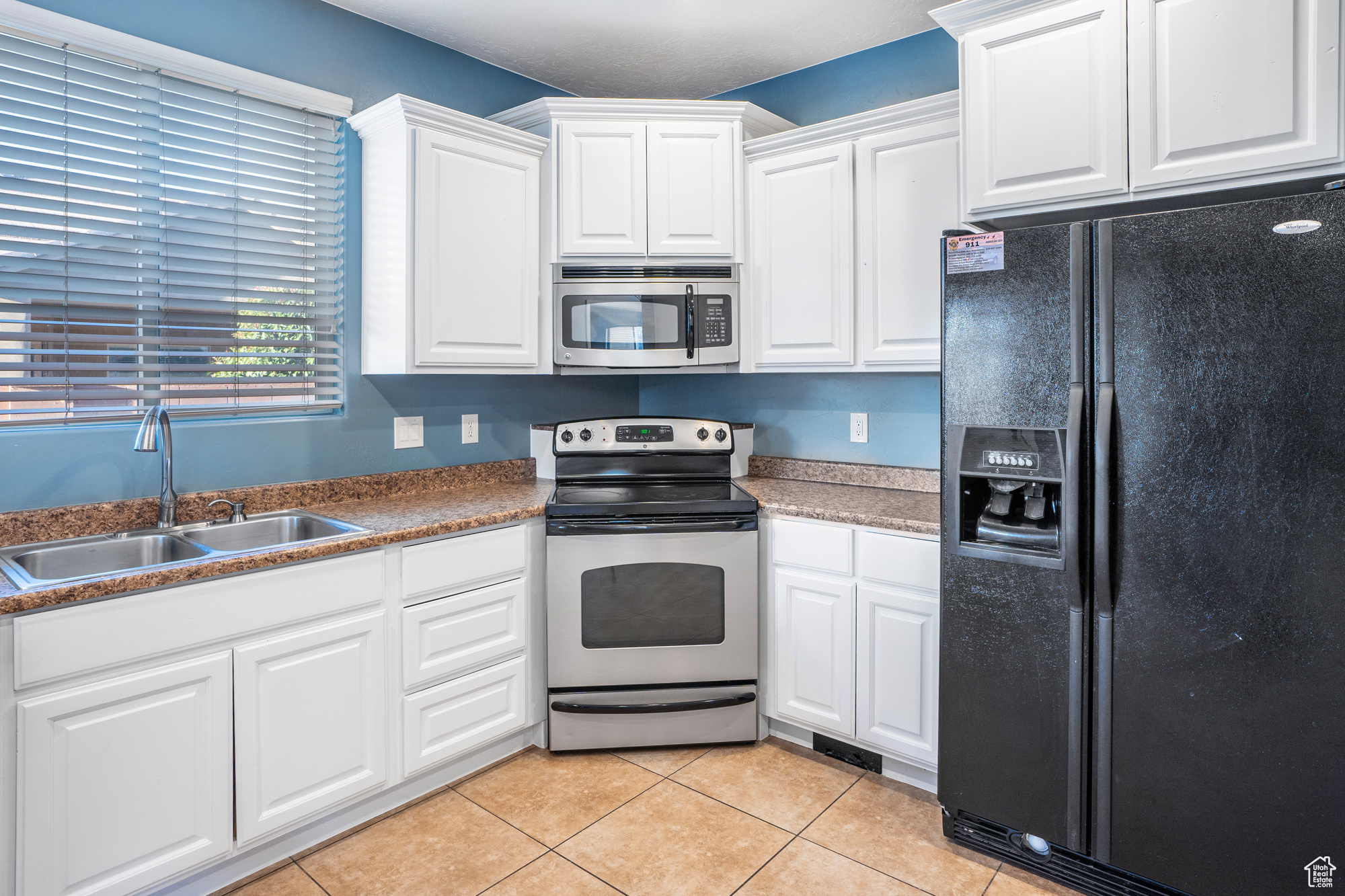 Kitchen with appliances with stainless steel finishes, sink, white cabinetry, and light tile patterned flooring