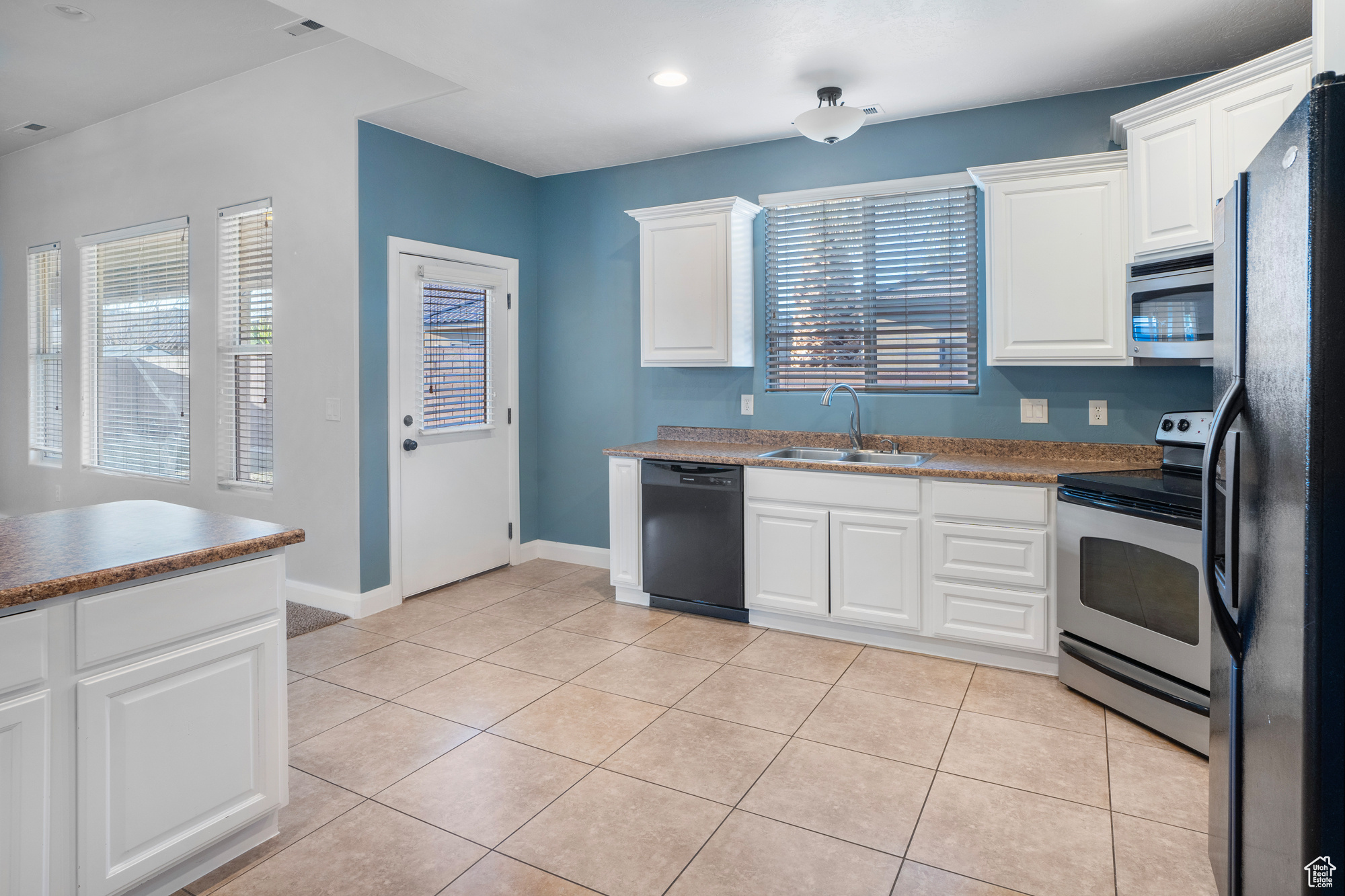 Kitchen with light tile patterned flooring, sink, white cabinets, and black appliances