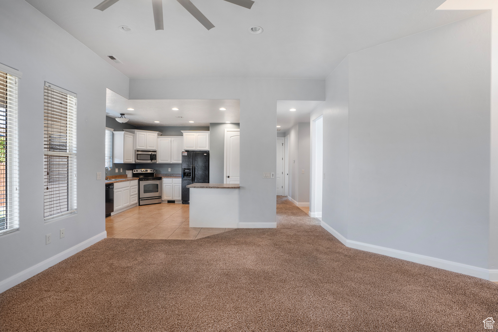 Kitchen with black appliances, white cabinets, a wealth of natural light, and light colored carpet