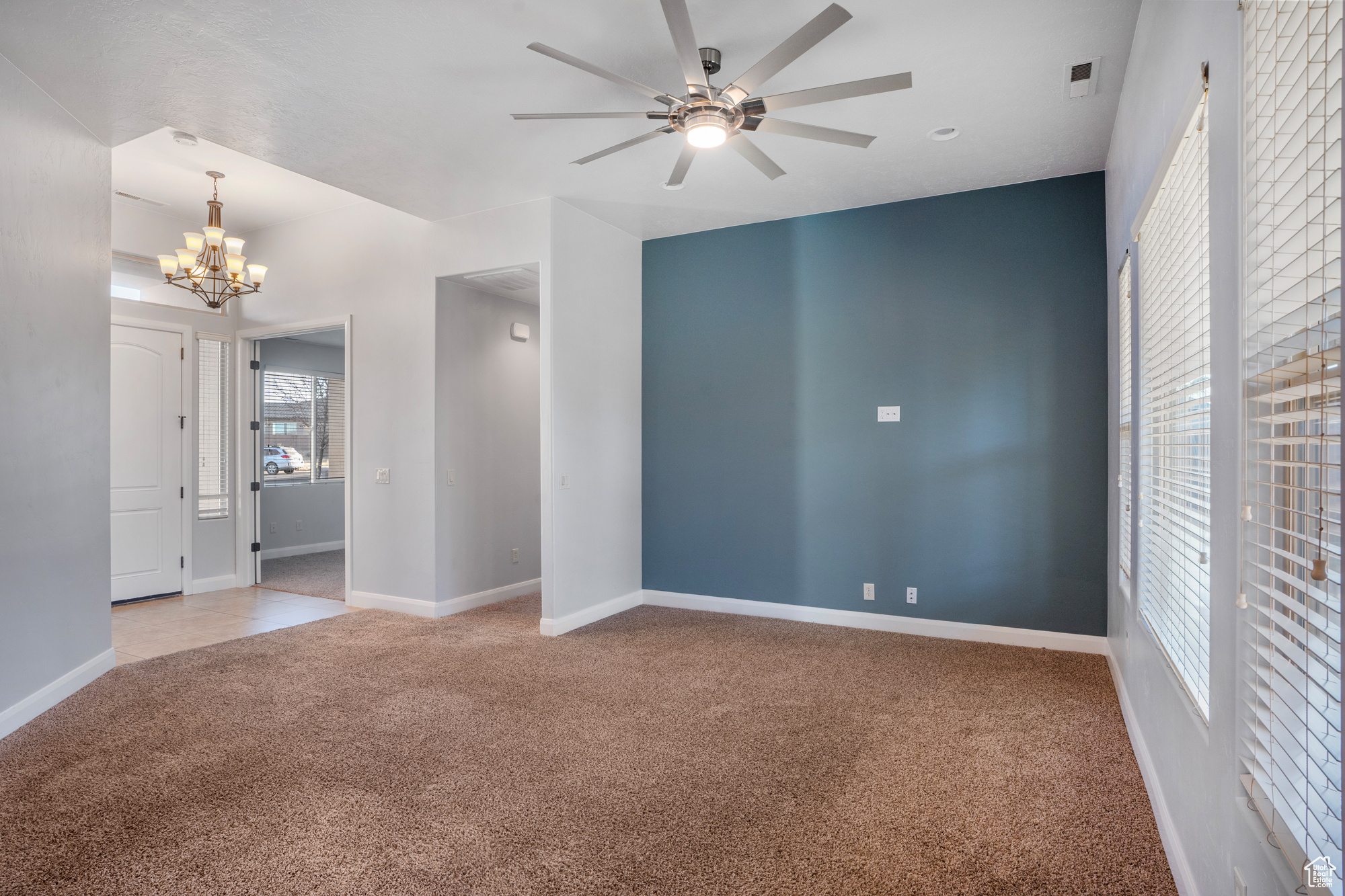 Carpeted spare room with ceiling fan with notable chandelier