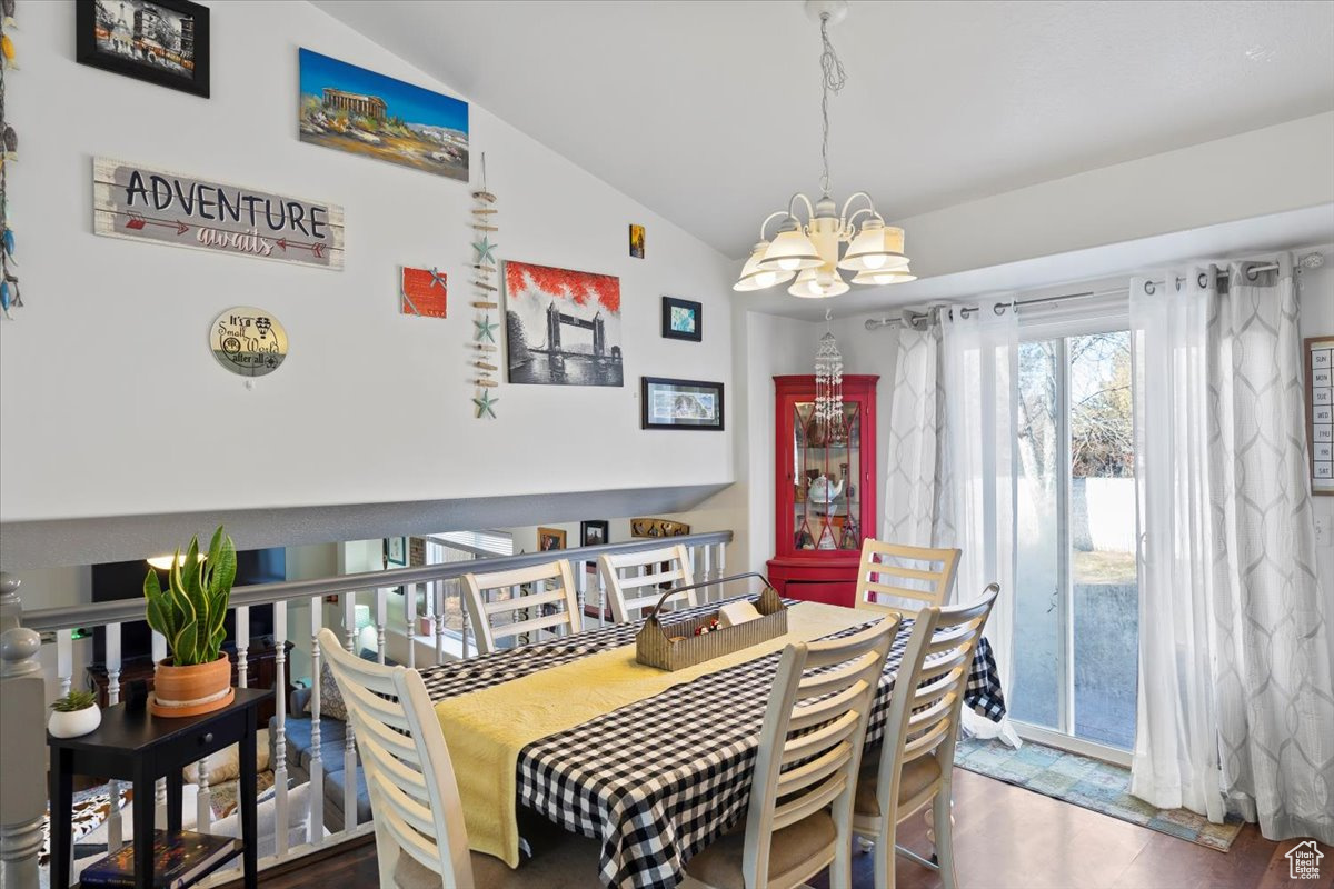 Dining space with hardwood / wood-style floors, a notable chandelier, and vaulted ceiling