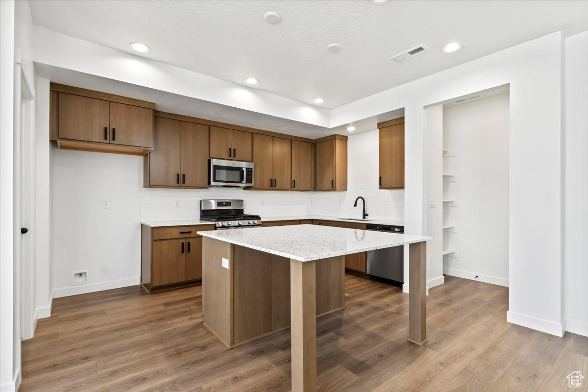 Kitchen with appliances with stainless steel finishes, sink, hardwood / wood-style flooring, light stone counters, and a center island