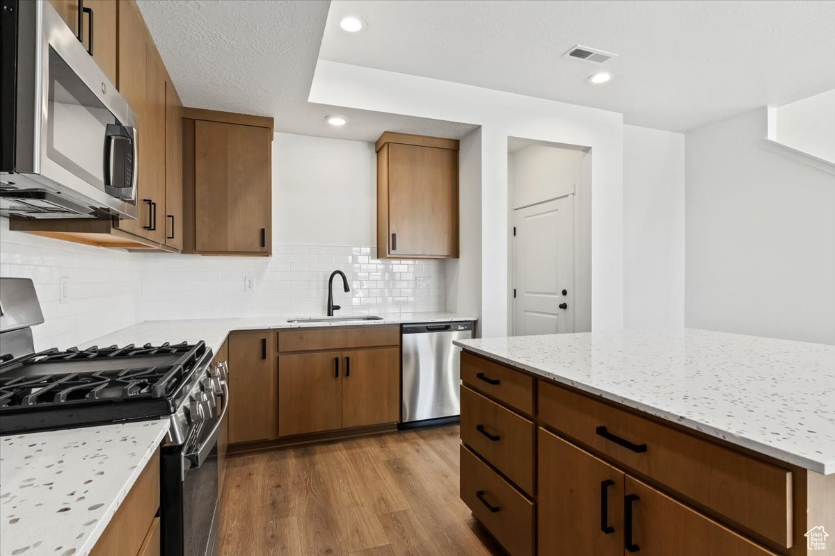 Kitchen featuring light hardwood / wood-style flooring, appliances with stainless steel finishes, sink, backsplash, and light stone countertops