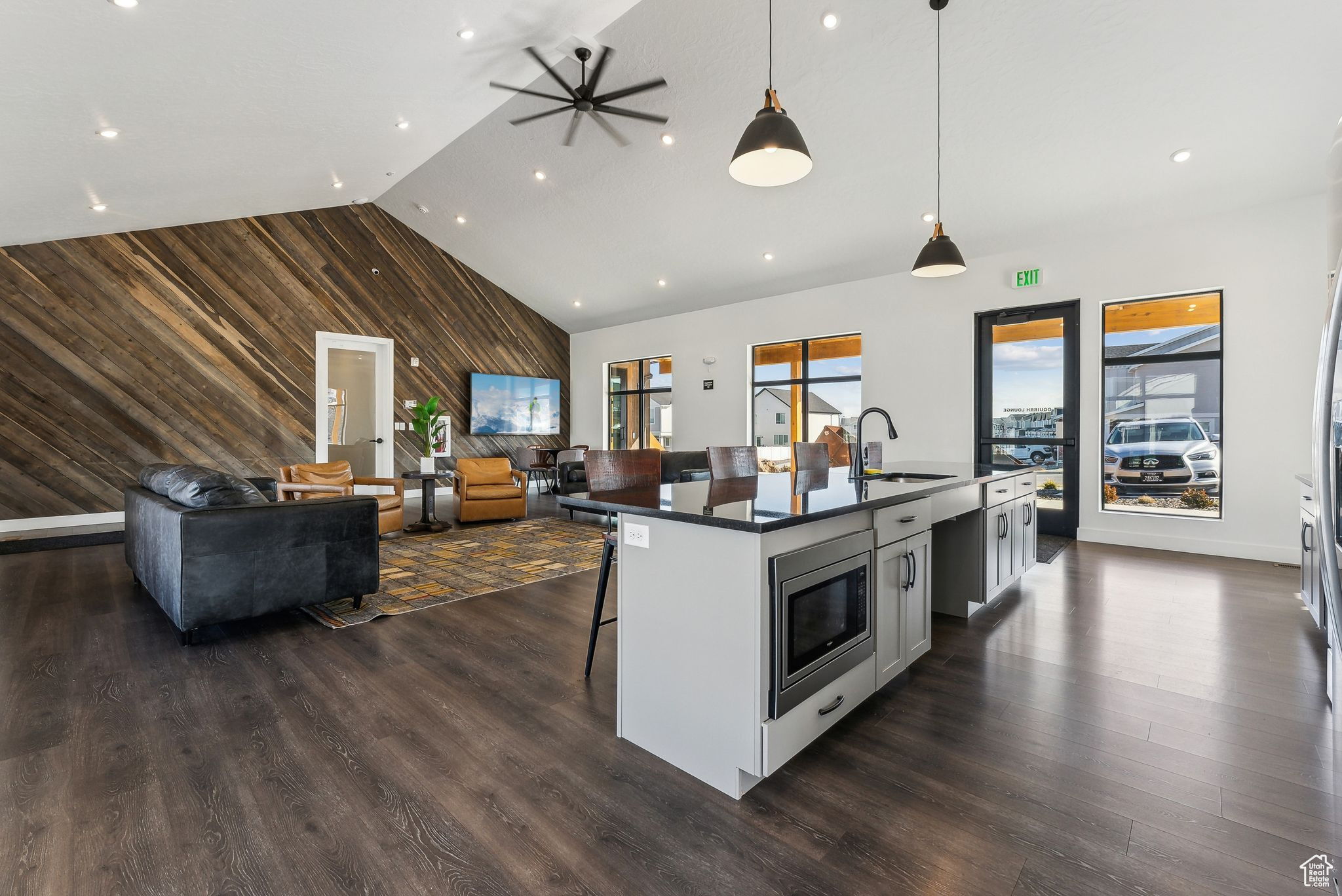 Kitchen featuring stainless steel microwave, hanging light fixtures, an island with sink, wood walls, and a breakfast bar area