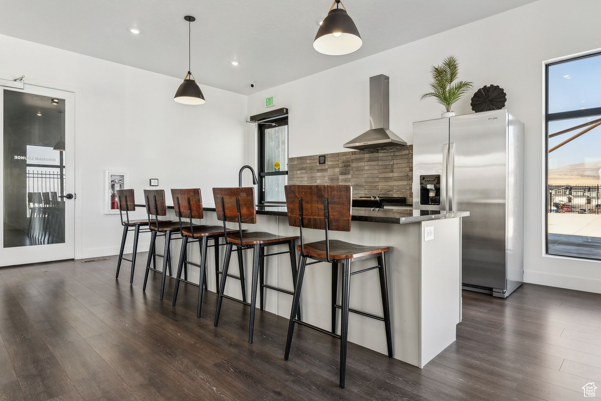 Kitchen featuring tasteful backsplash, a kitchen breakfast bar, wall chimney range hood, decorative light fixtures, and stainless steel fridge