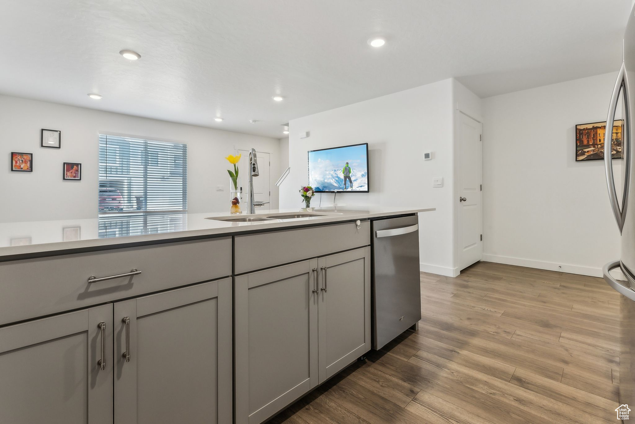 Kitchen with sink, stainless steel dishwasher, gray cabinetry, and wood-type flooring