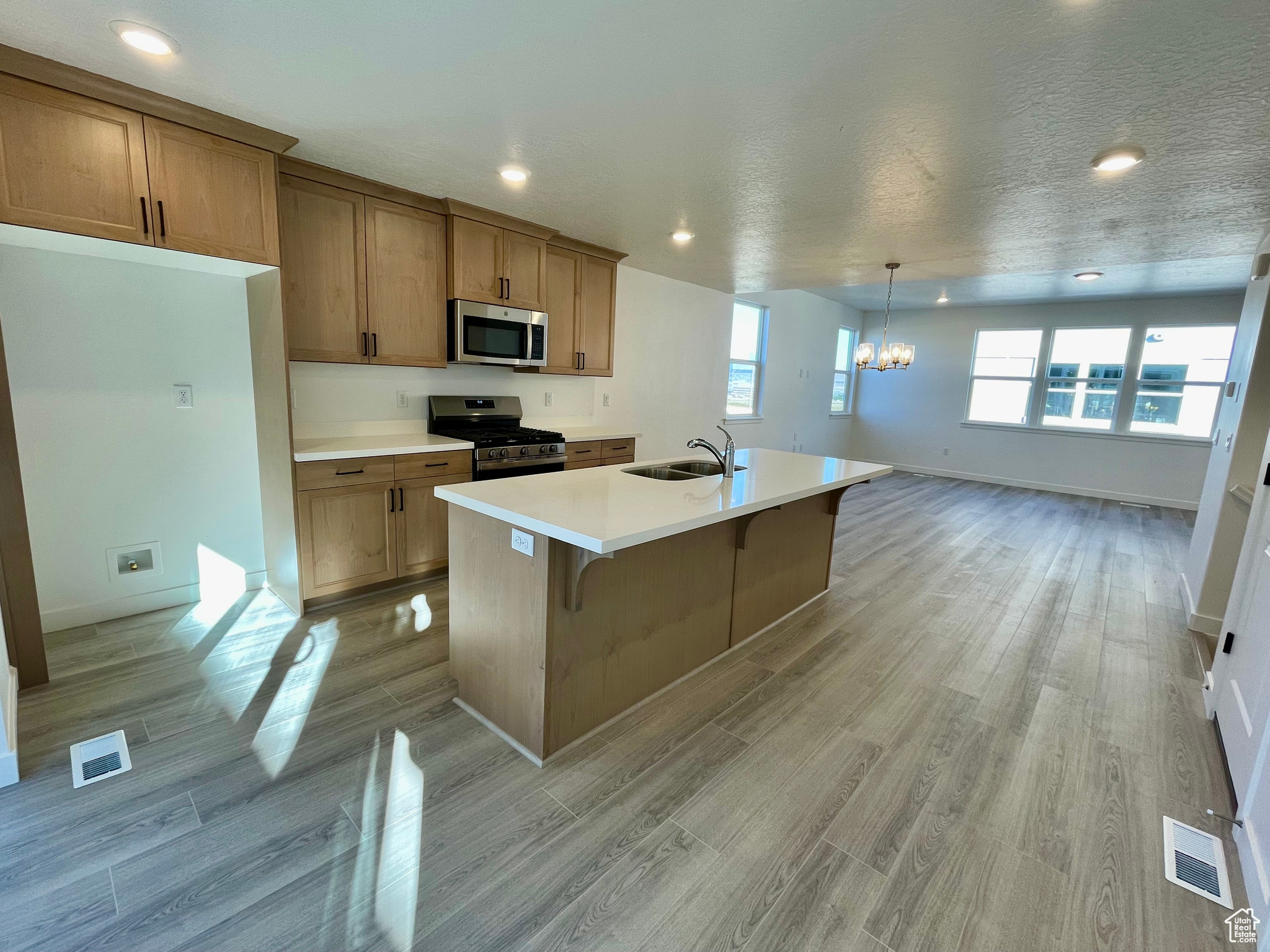 Kitchen featuring a textured ceiling, appliances with stainless steel finishes, decorative light fixtures, sink, and a kitchen island with sink