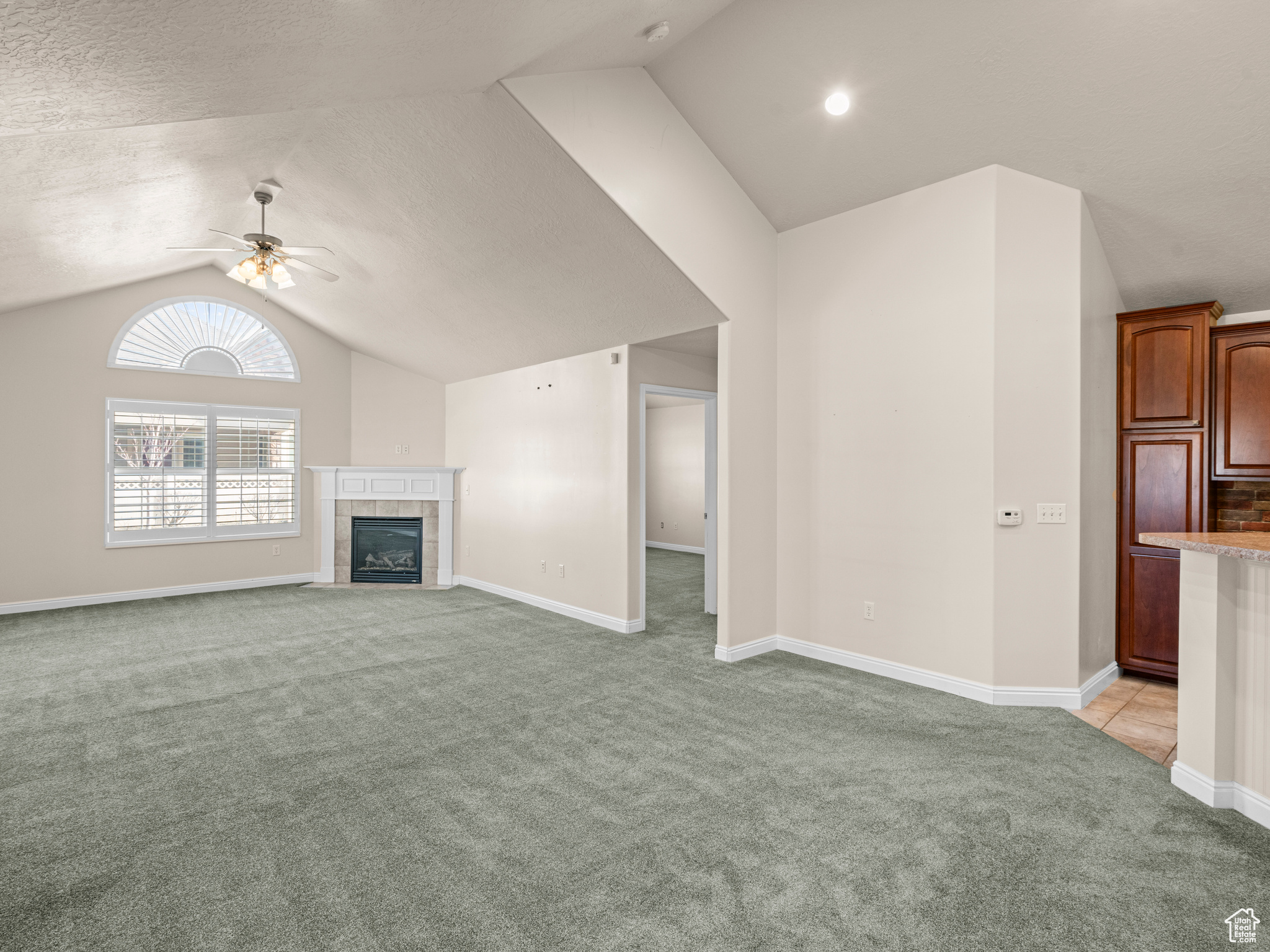 Unfurnished living room featuring a tiled fireplace, light colored carpet, vaulted ceiling, and ceiling fan