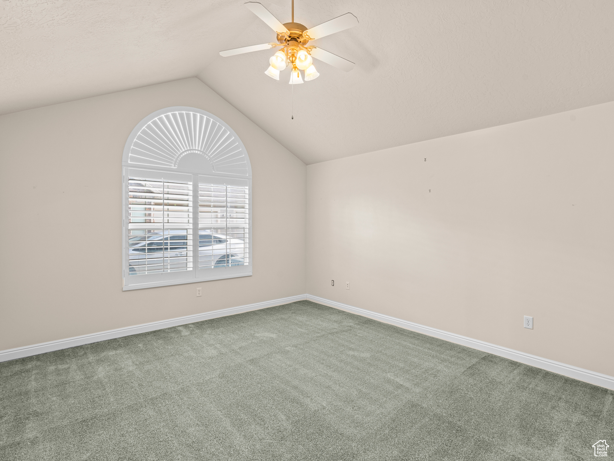 Carpeted spare room with ceiling fan and vaulted ceiling