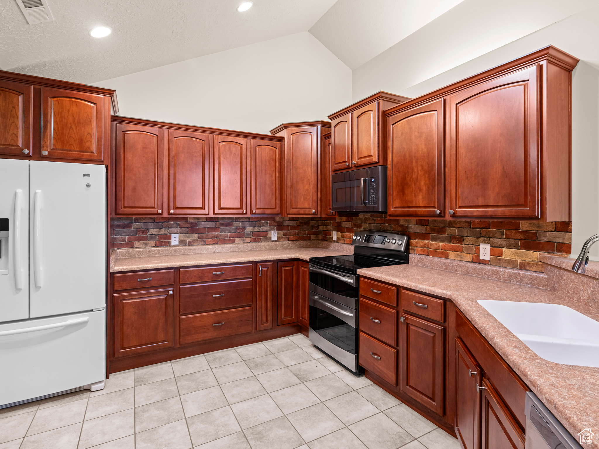 Kitchen with decorative backsplash, sink, appliances with stainless steel finishes, and light tile patterned flooring