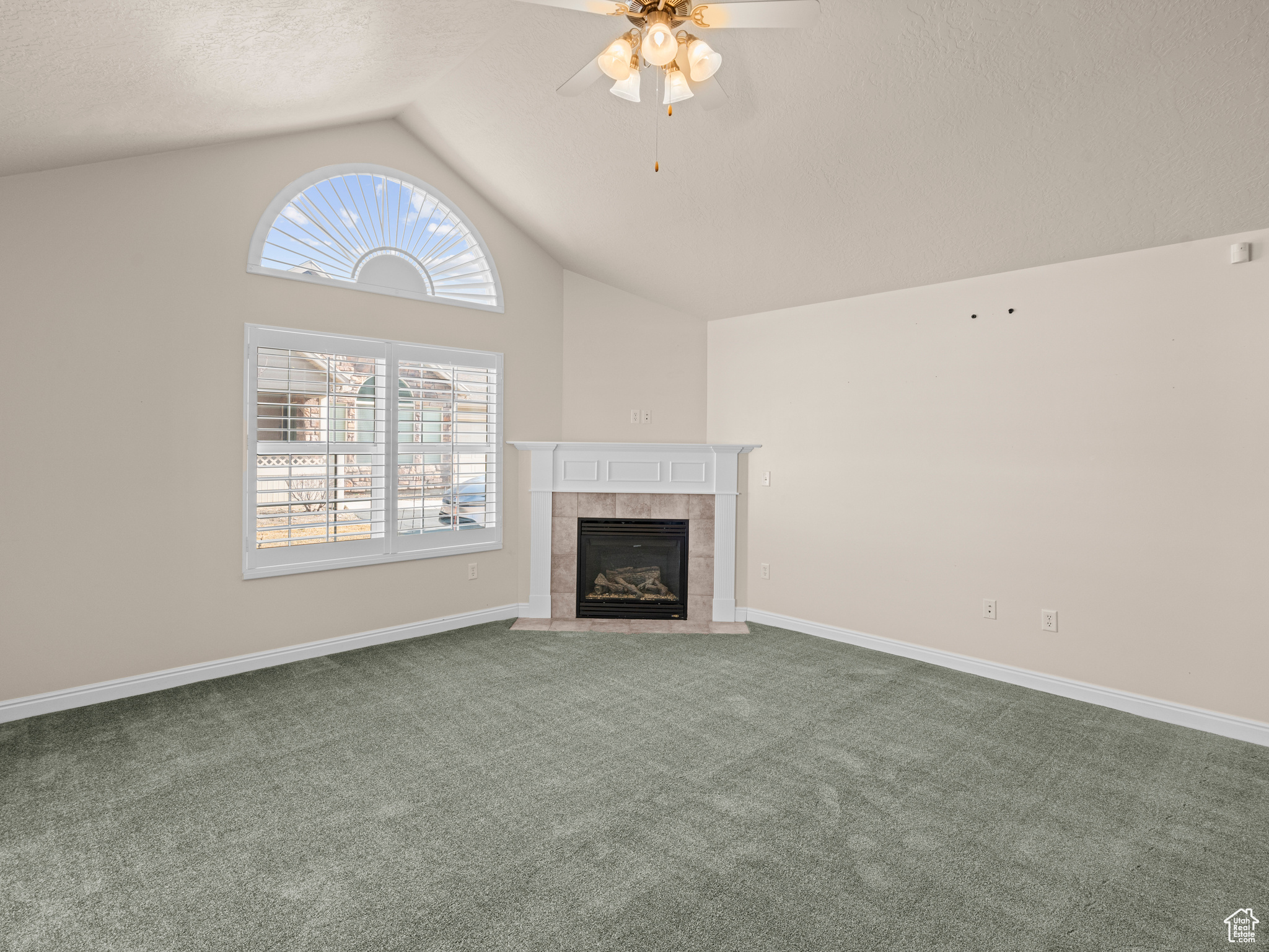Unfurnished living room with a textured ceiling, lofted ceiling, carpet flooring, ceiling fan, and a tiled fireplace