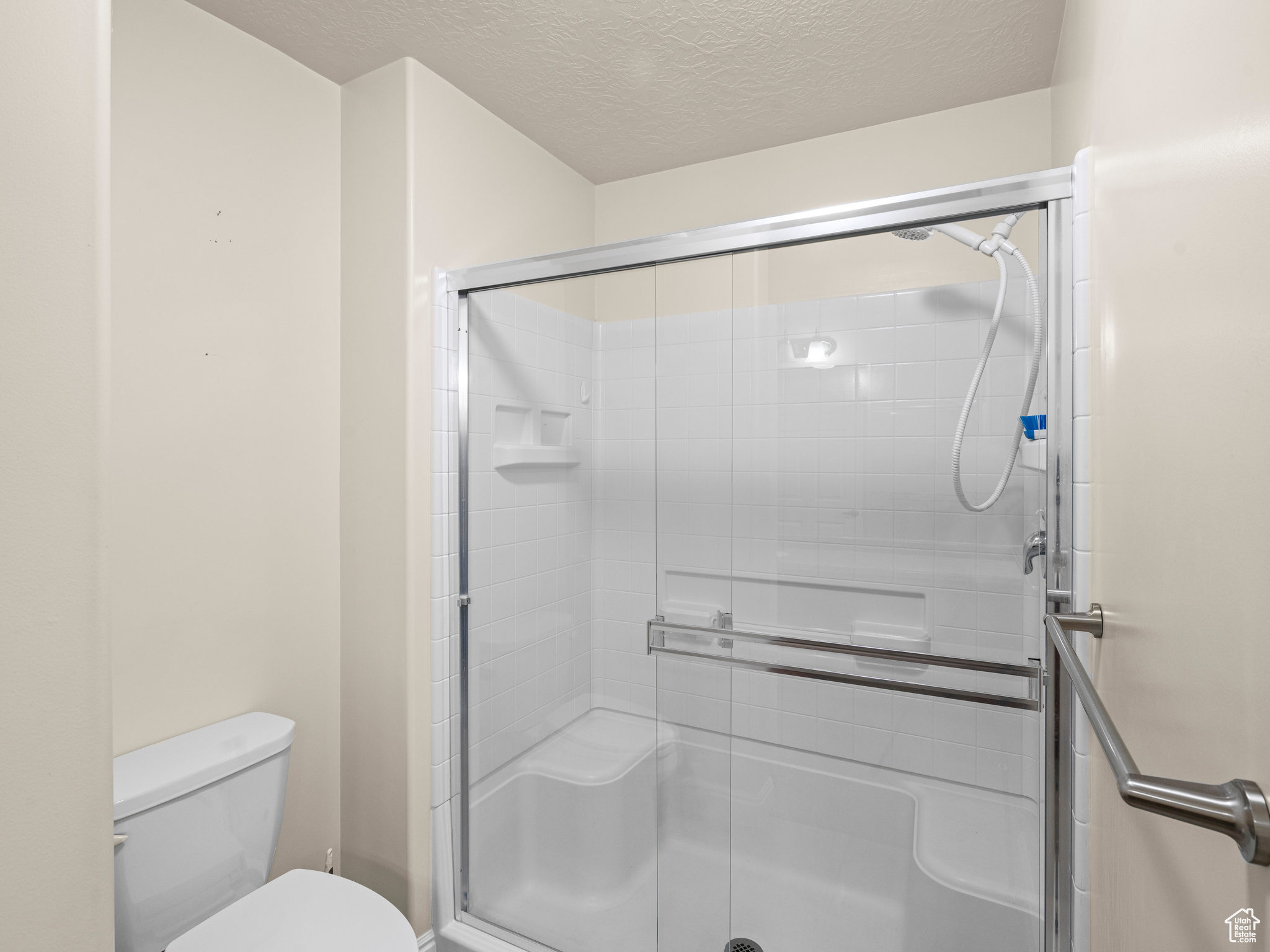 Bathroom featuring toilet, a textured ceiling, and a shower with shower door