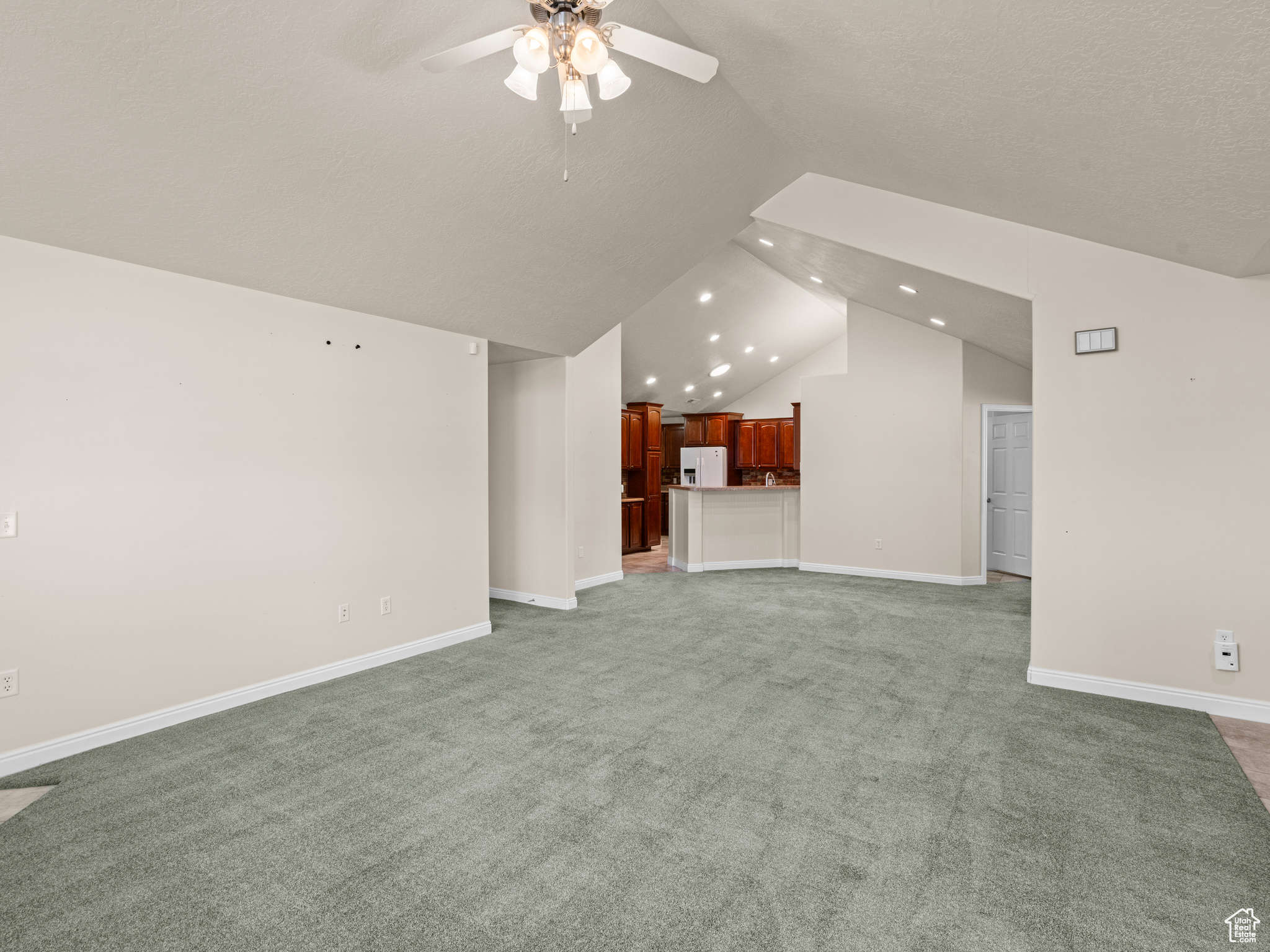 Unfurnished living room featuring ceiling fan, carpet, and lofted ceiling