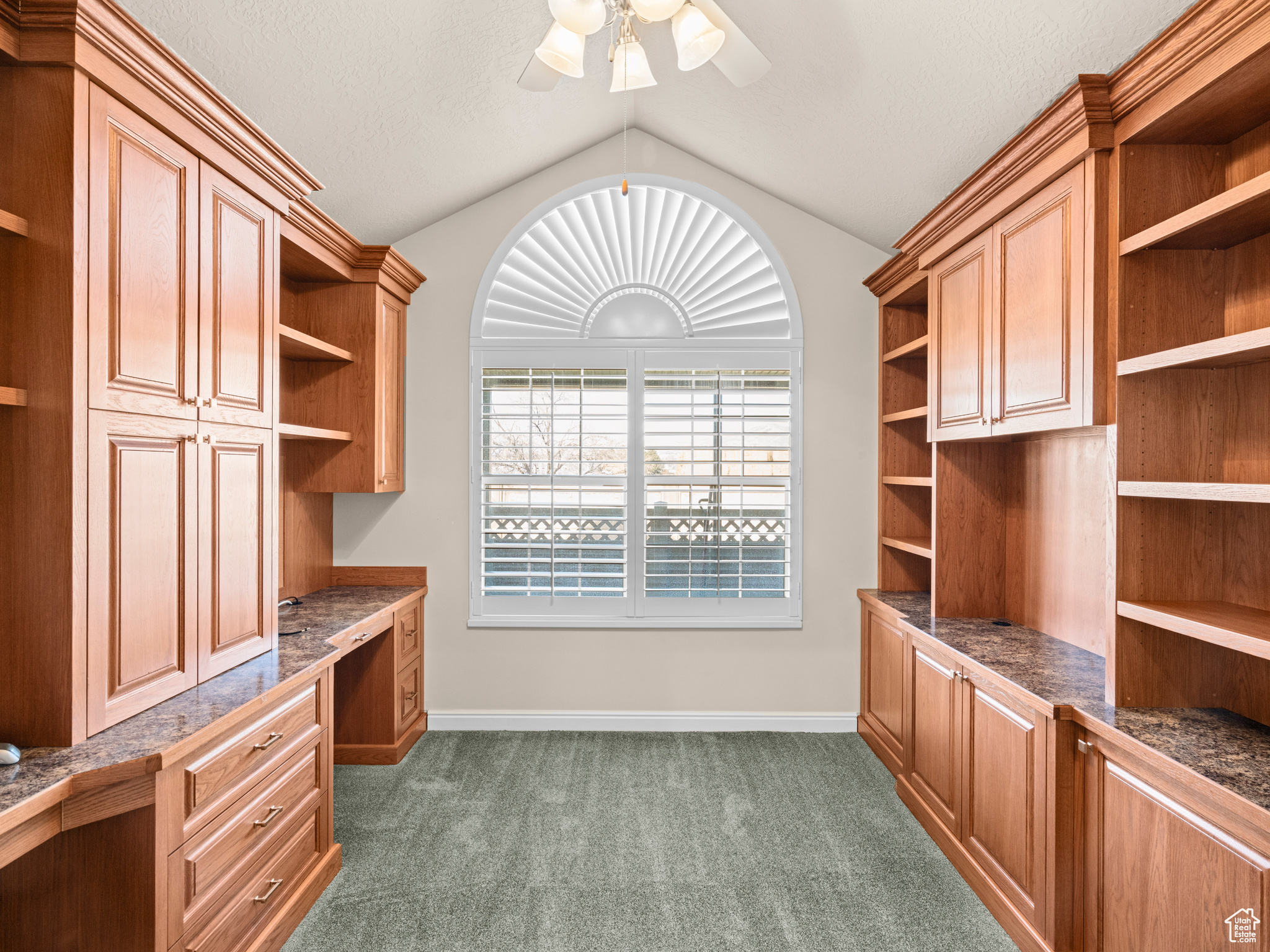 Unfurnished office featuring ceiling fan, lofted ceiling, dark carpet, and built in desk