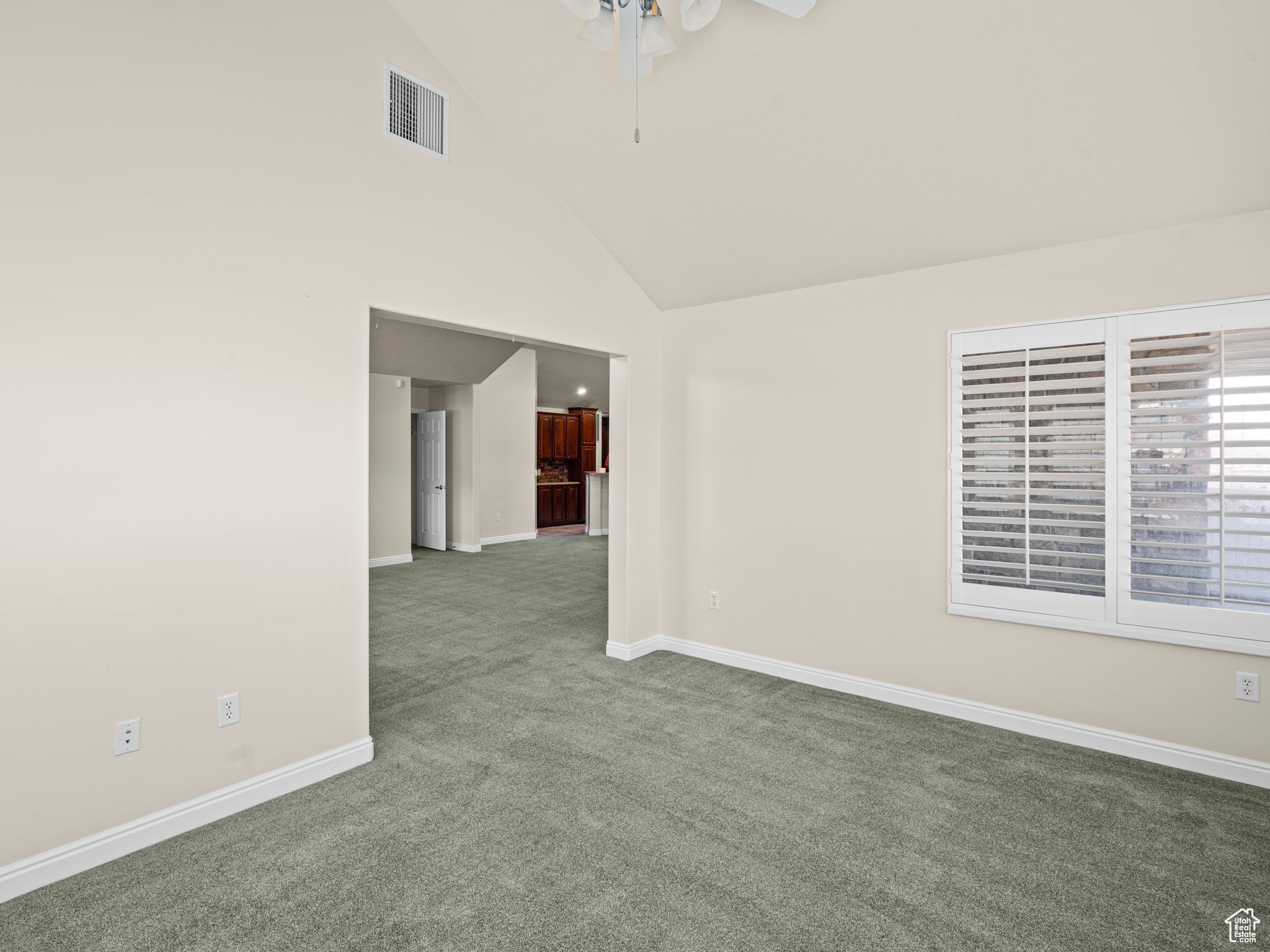 Carpeted empty room featuring ceiling fan and high vaulted ceiling