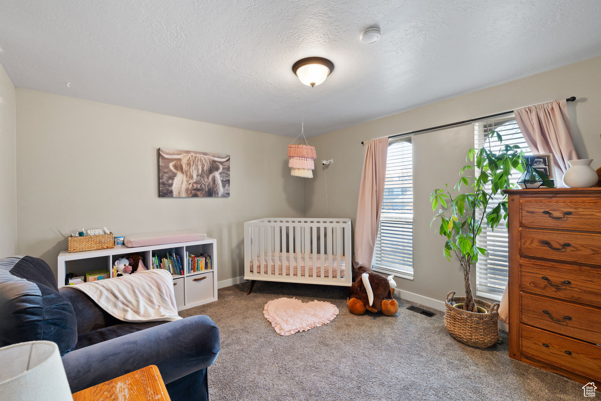 Carpeted bedroom with radiator heating unit, a crib, and a textured ceiling