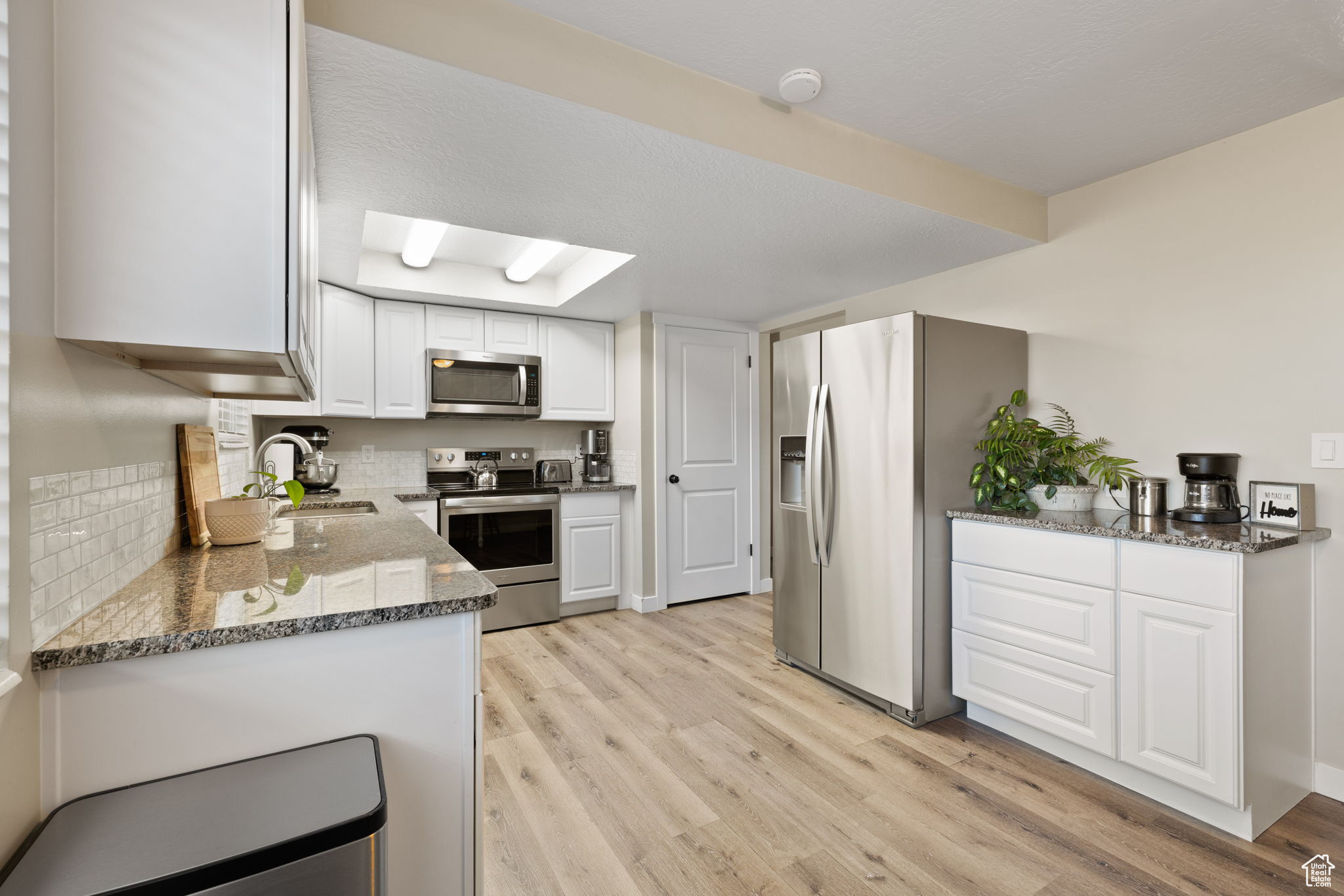 Kitchen featuring appliances with stainless steel finishes, white cabinetry, sink, light wood-type flooring, and dark stone countertops