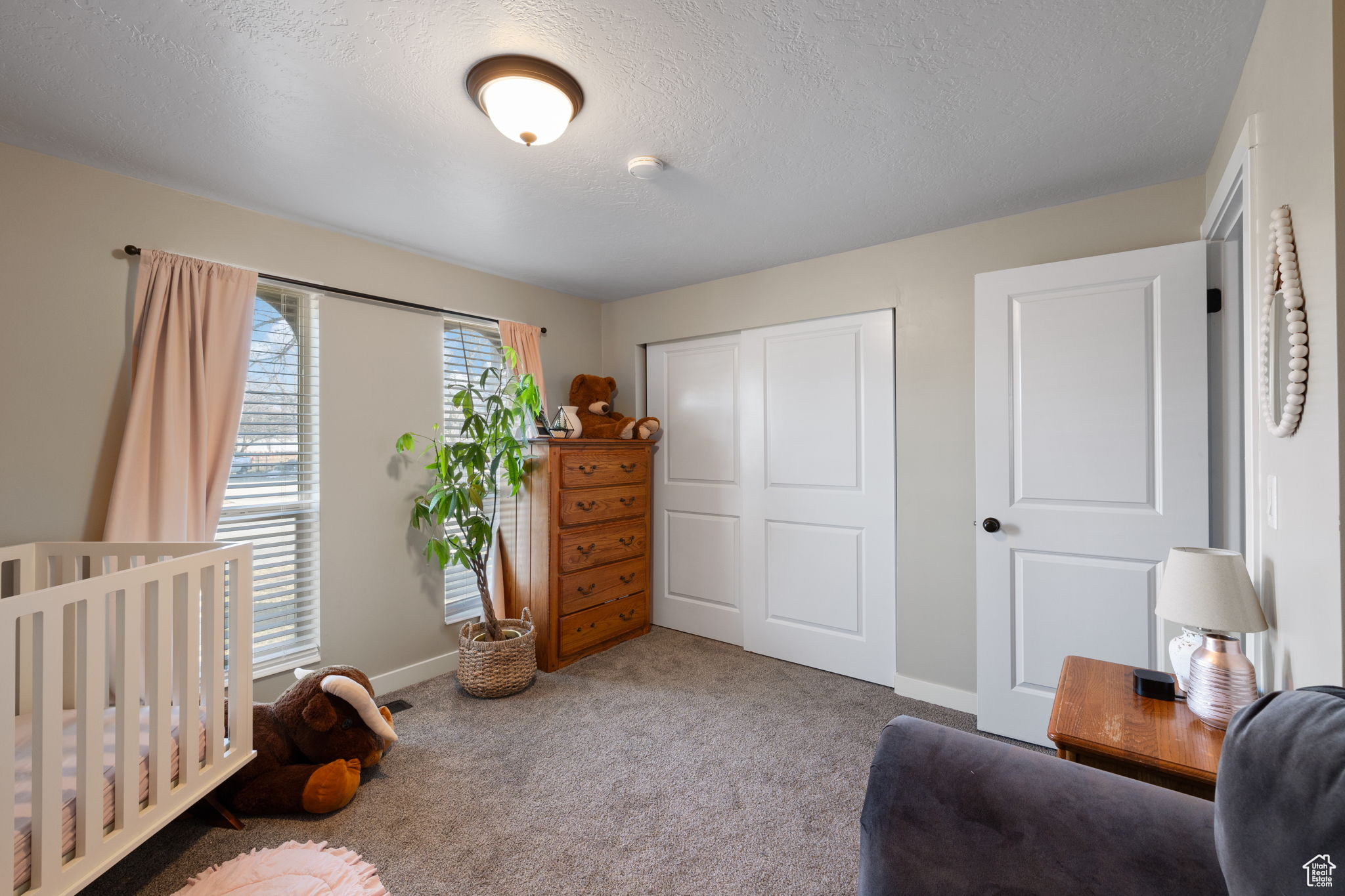 Bedroom with a textured ceiling, carpet flooring, a closet, and a nursery area