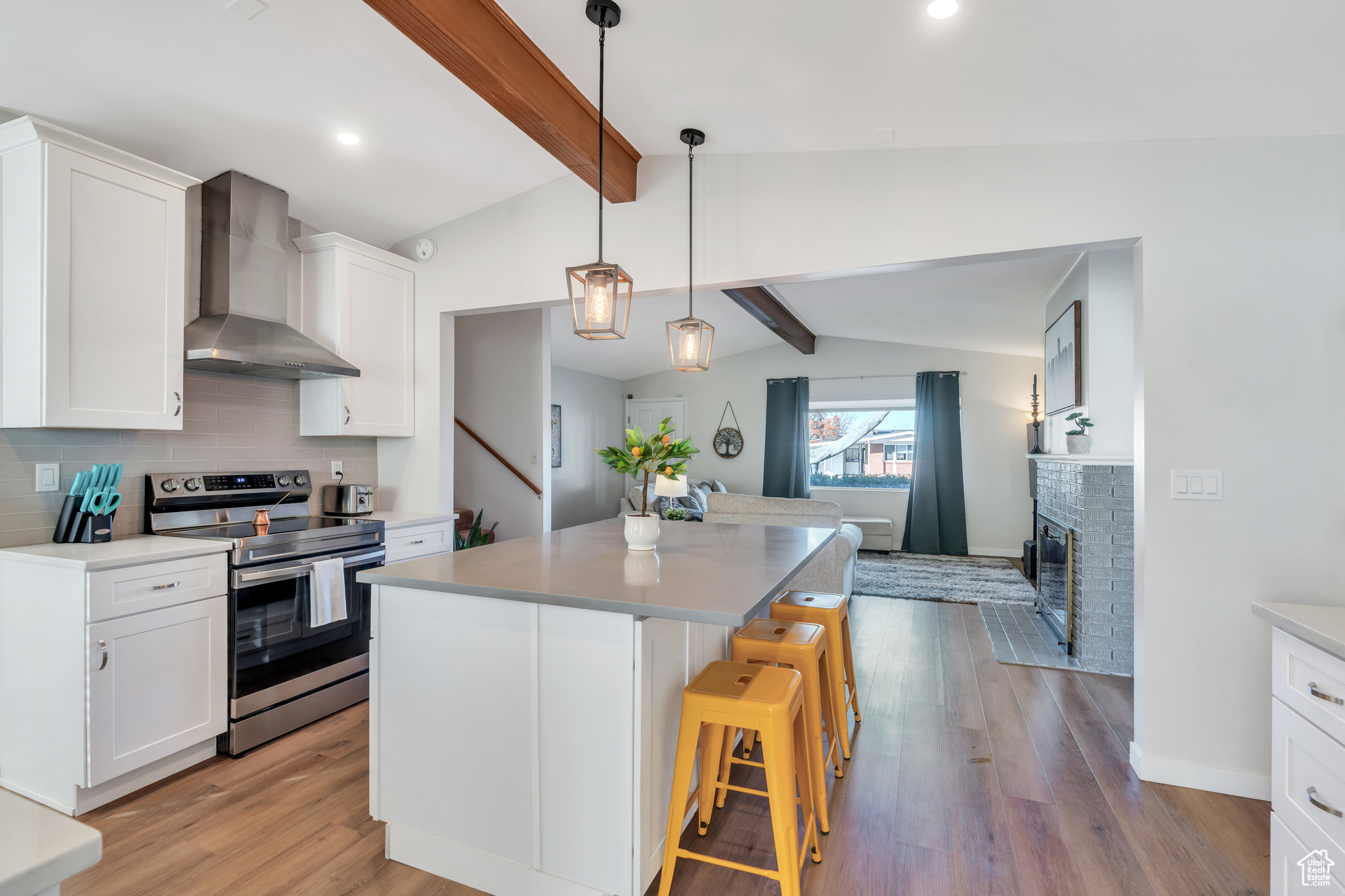 Kitchen featuring a kitchen island, lofted ceiling with beams, white cabinets, wall chimney range hood, and stainless steel electric range