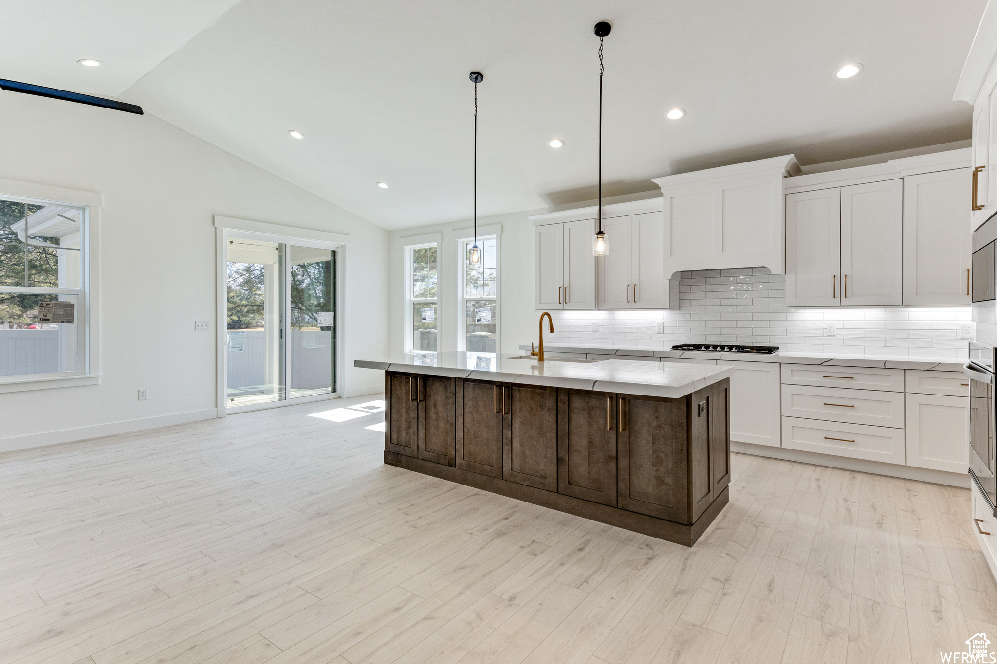 Kitchen featuring lofted ceiling, sink, hanging light fixtures, a kitchen island with sink, and gas stovetop