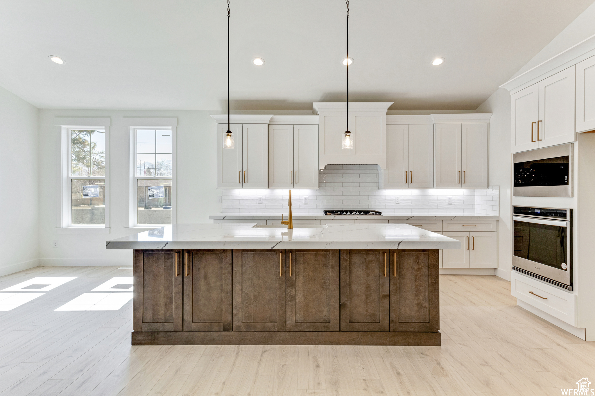 Kitchen featuring white cabinetry, light stone counters, hanging light fixtures, oven, and a kitchen island with sink