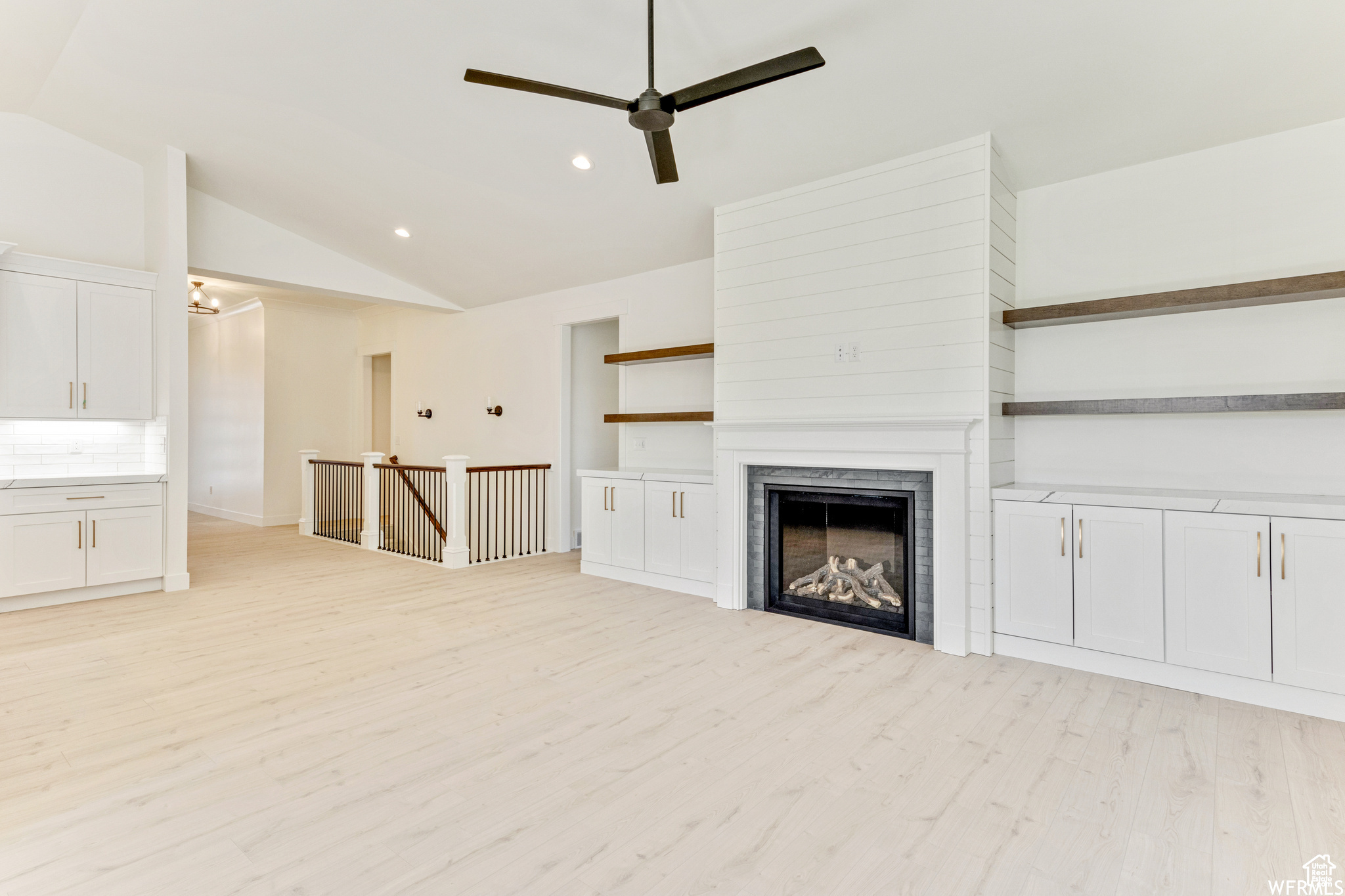 Unfurnished living room featuring lofted ceiling, ceiling fan, and light wood-type flooring