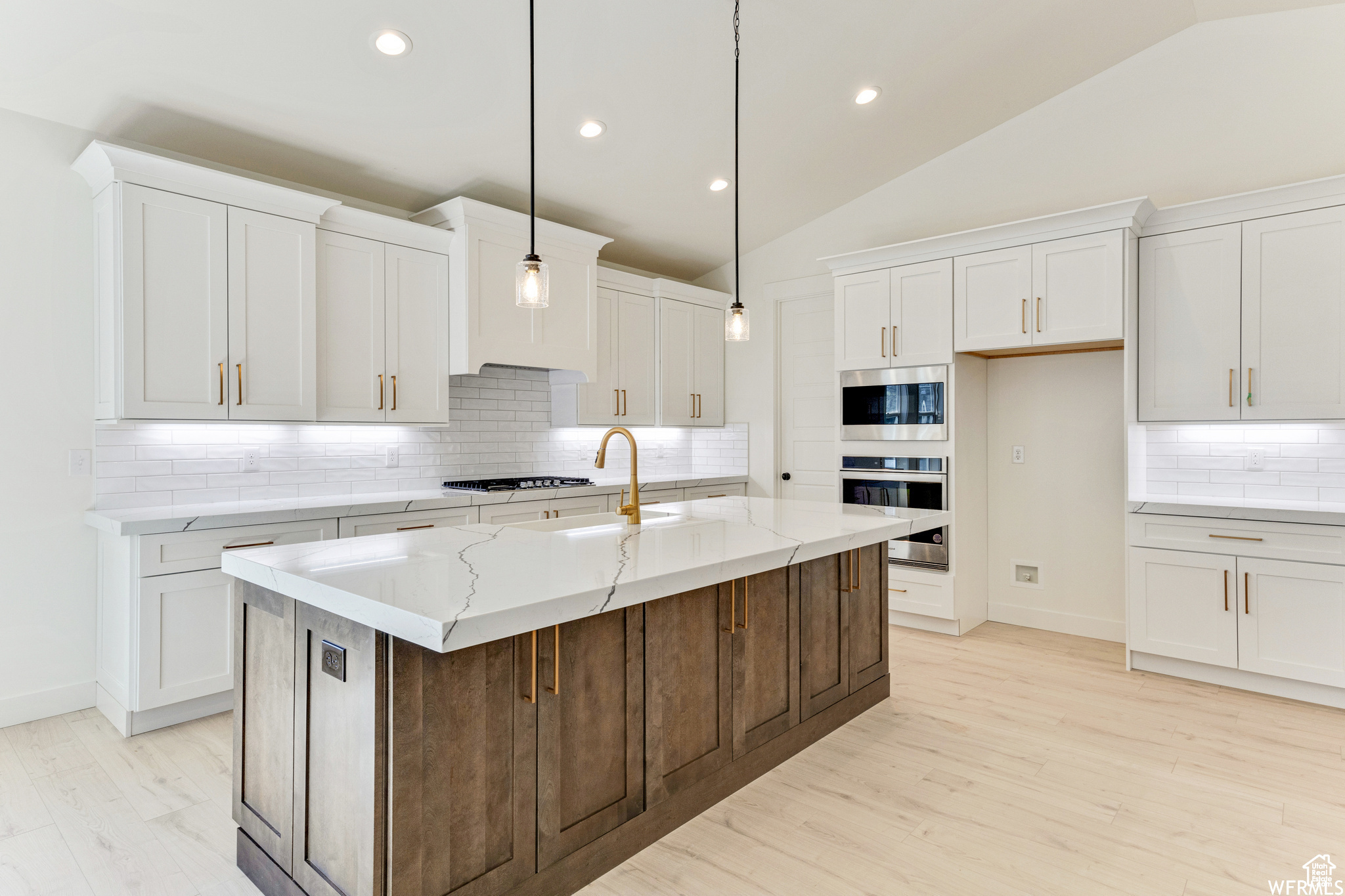 Kitchen with lofted ceiling, sink, white cabinets, hanging light fixtures, and a center island with sink