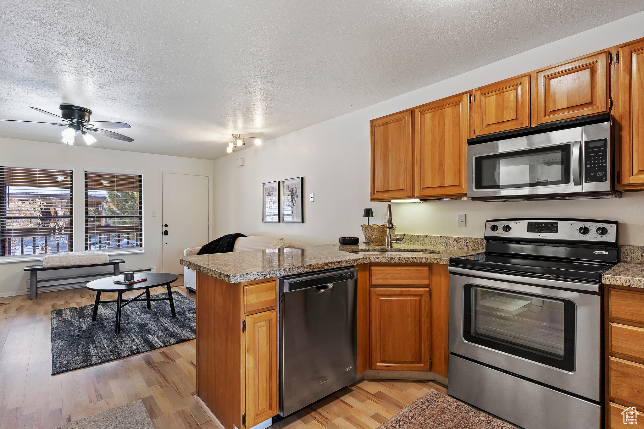 Kitchen with sink, light hardwood / wood-style floors, kitchen peninsula, stainless steel appliances, and a textured ceiling