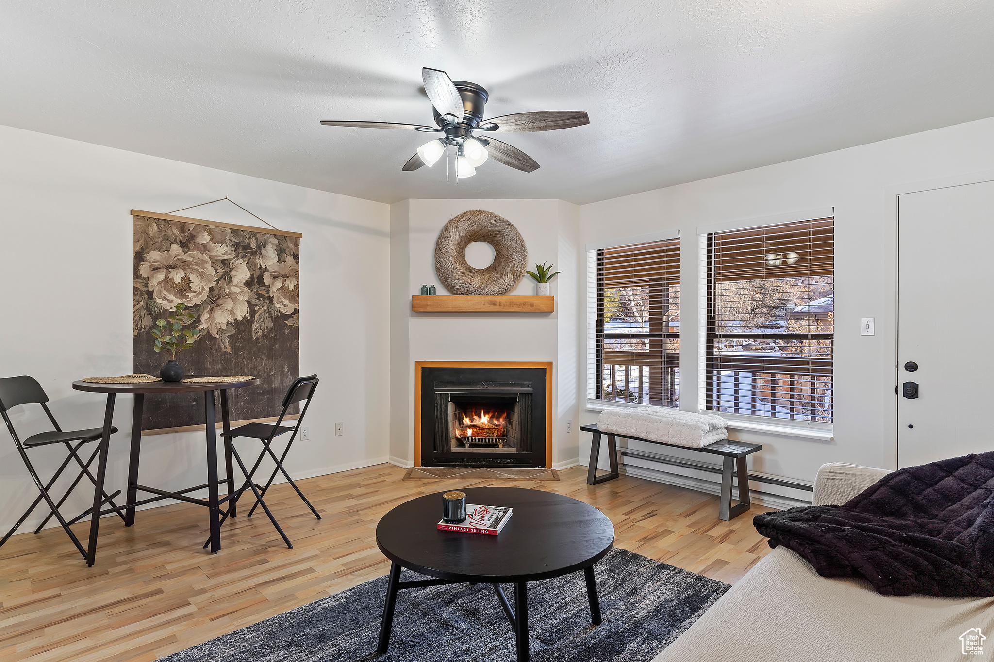 Living room with ceiling fan, a textured ceiling, baseboard heating, and light wood-type flooring