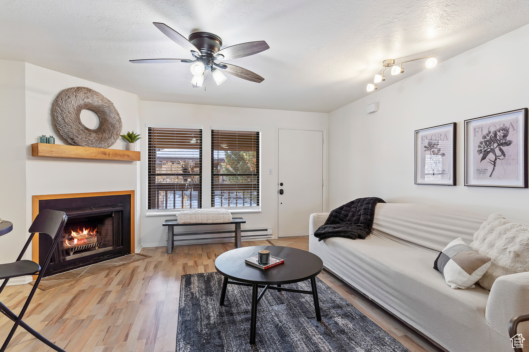 Living room featuring ceiling fan, a baseboard heating unit, a textured ceiling, and light wood-type flooring