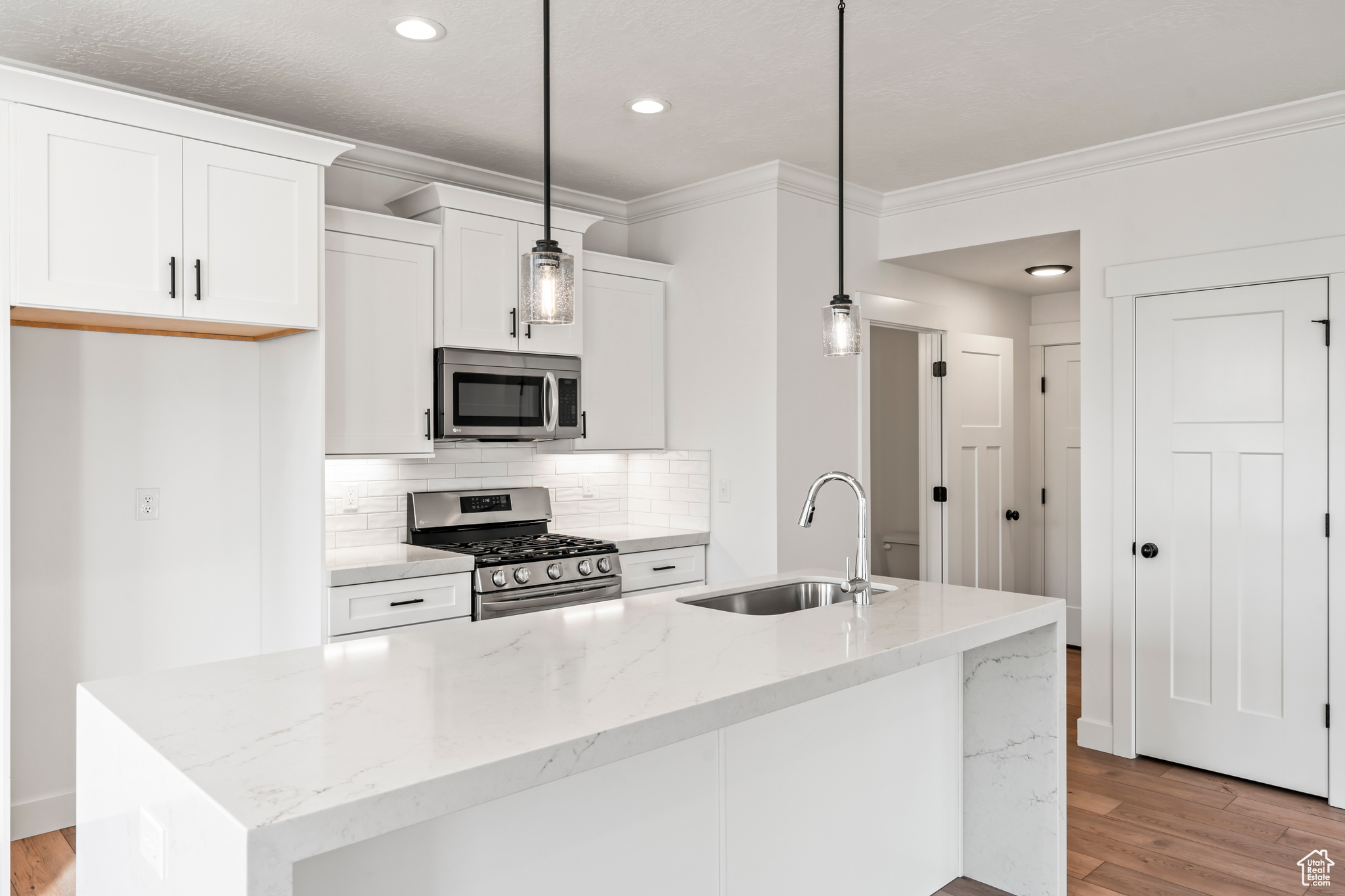 Kitchen with stainless steel appliances, decorative light fixtures, sink, and a center island with sink