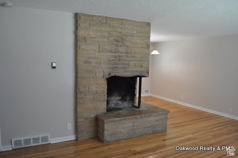 Living room with a stone fireplace, hardwood / wood-style floors, and a textured ceiling