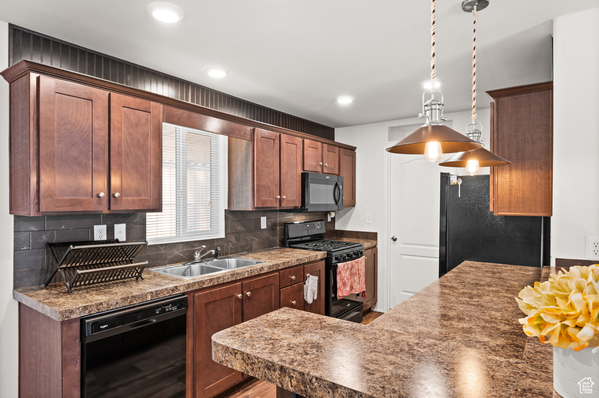 Kitchen with sink, pendant lighting, decorative backsplash, and black appliances