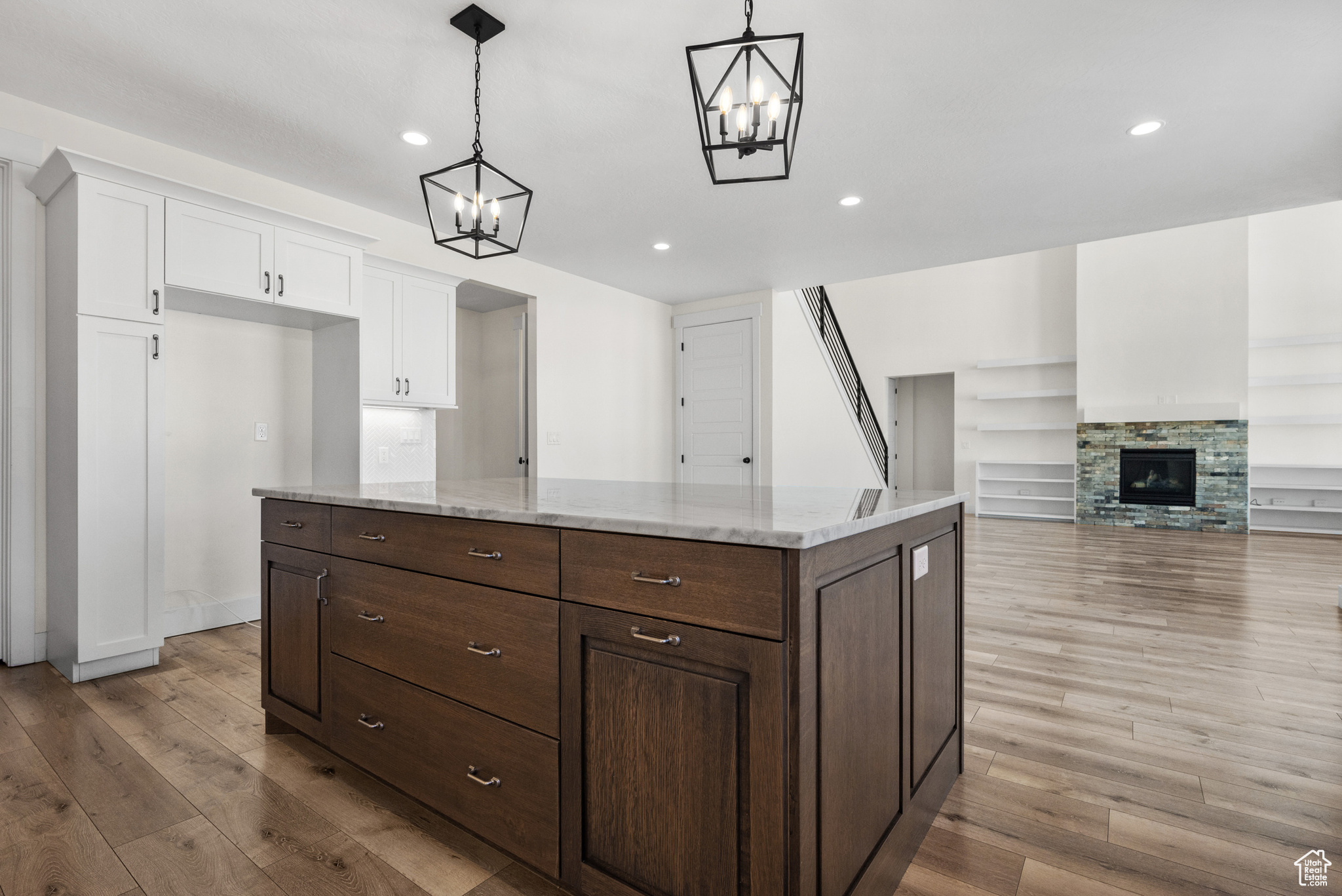 Kitchen featuring hanging light fixtures, a stone fireplace, white cabinets, and light hardwood / wood-style flooring