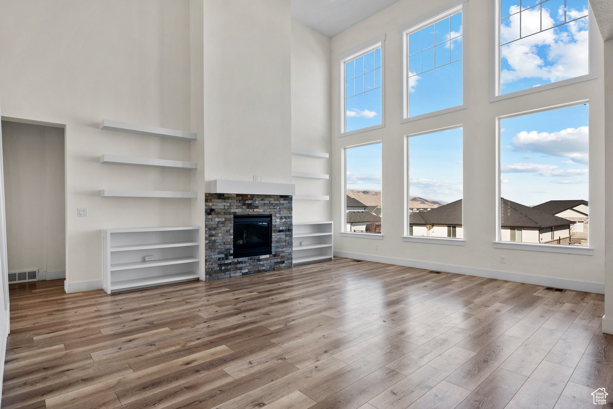 Unfurnished living room featuring hardwood / wood-style flooring, a stone fireplace, a high ceiling, and built in shelves